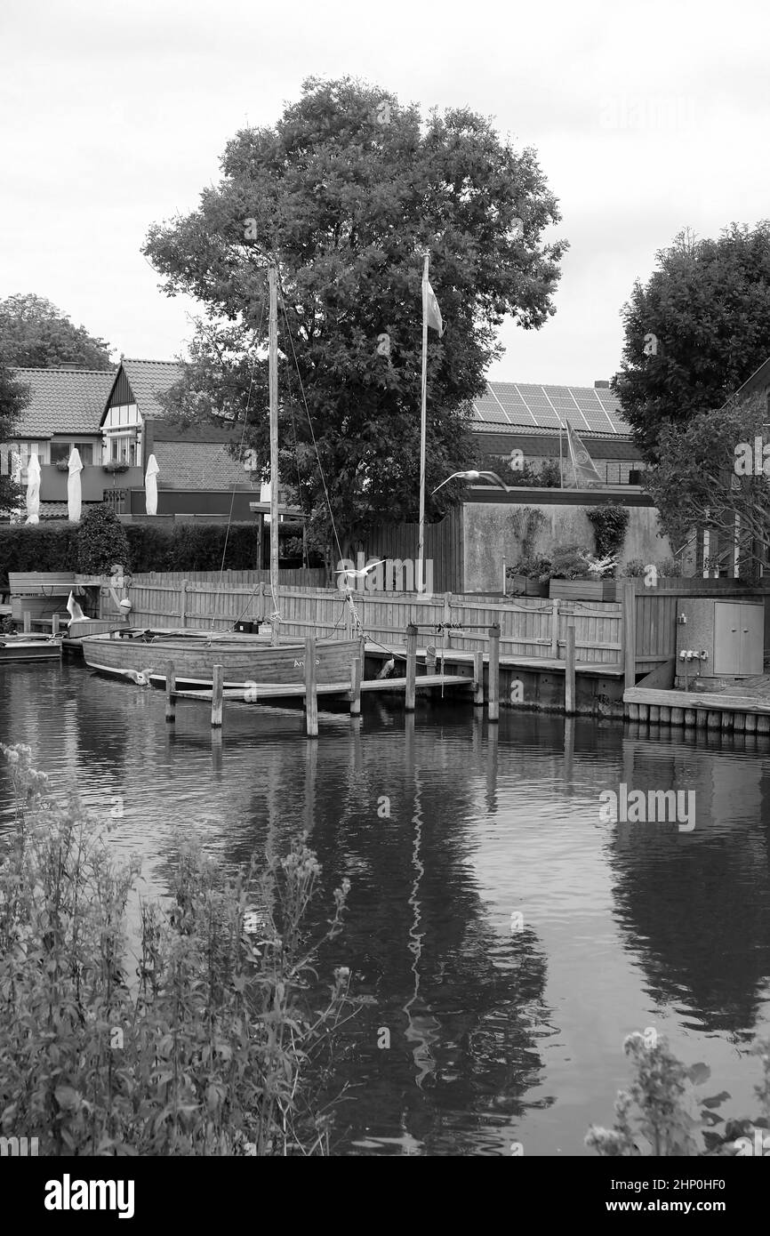 Schwarz-weiß Aufnahme eines Holzbootes auf einem See mit Häusern im Hintergrund Stockfoto