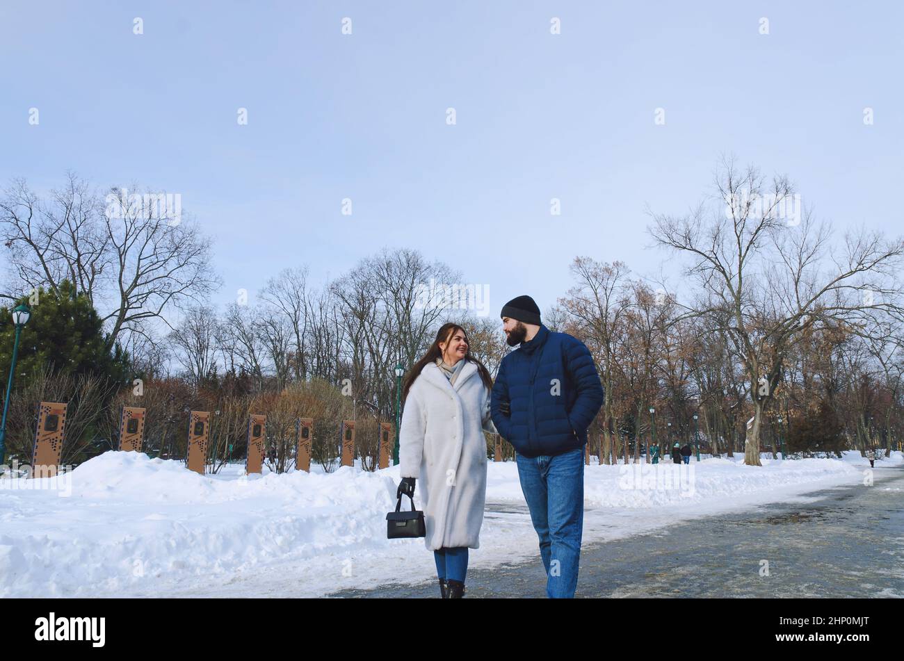 Ein Paar läuft in der Stadt. Junger Geschäftsmann in blauer Jacke mit Bart. Und eine niedliche Frau im langen Mantel. Familienurlaub und Zweisamkeit, Datum Stockfoto