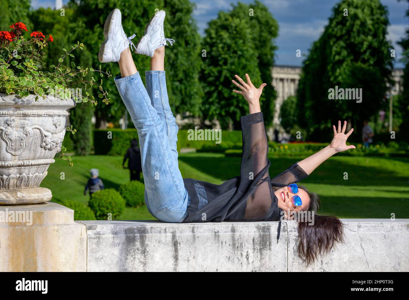 Ein sehr hübsches junges mongolisches Mädchen hat Spaß in einem Park und genießt die Sonne. Sie liegt auf ihrem Rücken an einer Wand. Stockfoto