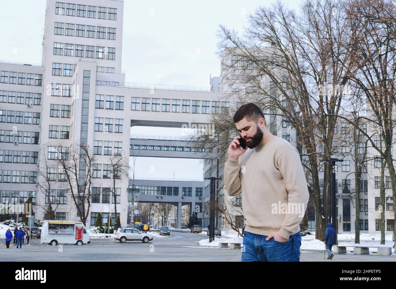 Junger eleganter Geschäftsmann in Winterkleidung, Jacke, Hut. In der Stadtstraße spazieren, telefonieren, Selfie machen. Arbeiten im Freien. Stockfoto