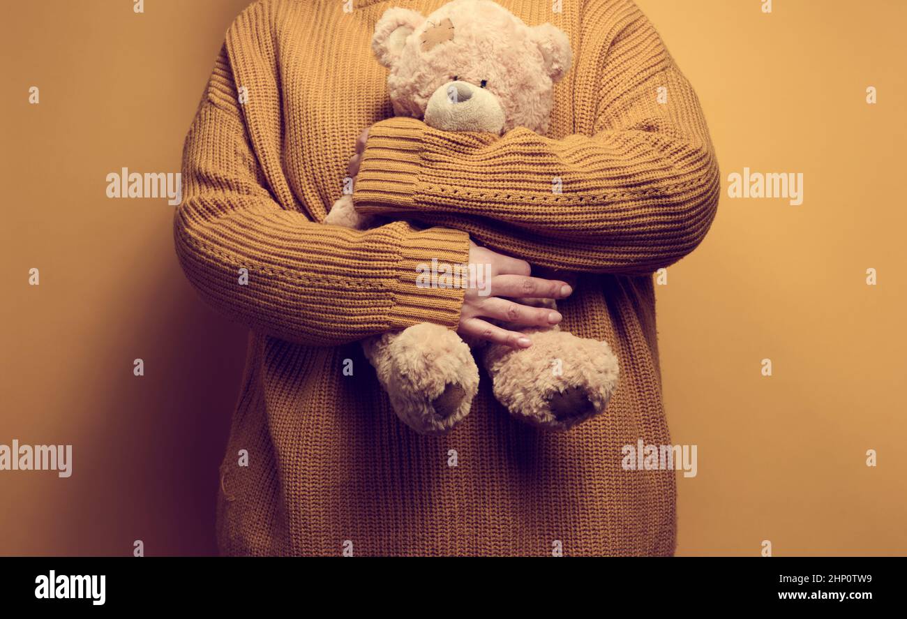 Frau in orange gestrickt Pullover Umarmungen niedlichen braunen Teddybär. Das Konzept von Einsamkeit und Traurigkeit, Depression Stockfoto