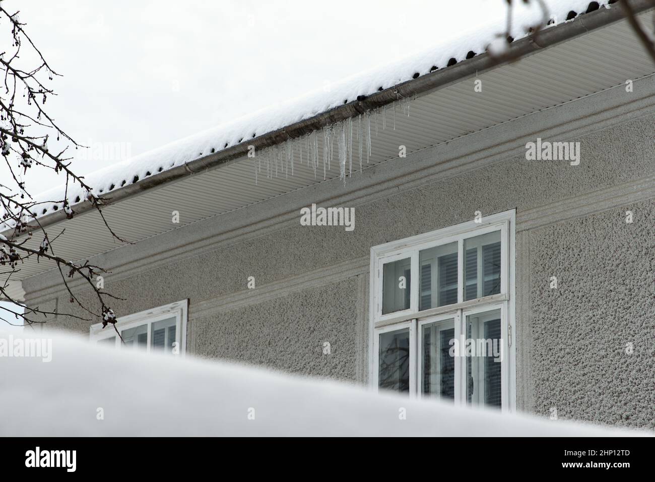 Eiszapfen hängen im Winter auf dem Schneedach eines Wohnhauses, was für die Gesundheit der Bewohner gefährlich ist Stockfoto