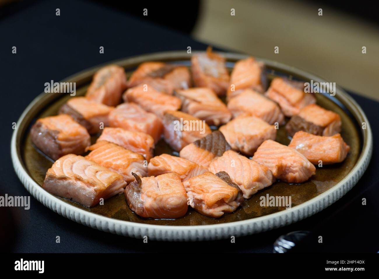 Gebratener Lachs in kleinen Stücken. Scheiben, Würfel. Nahaufnahme auf einer Keramikplatte Stockfoto