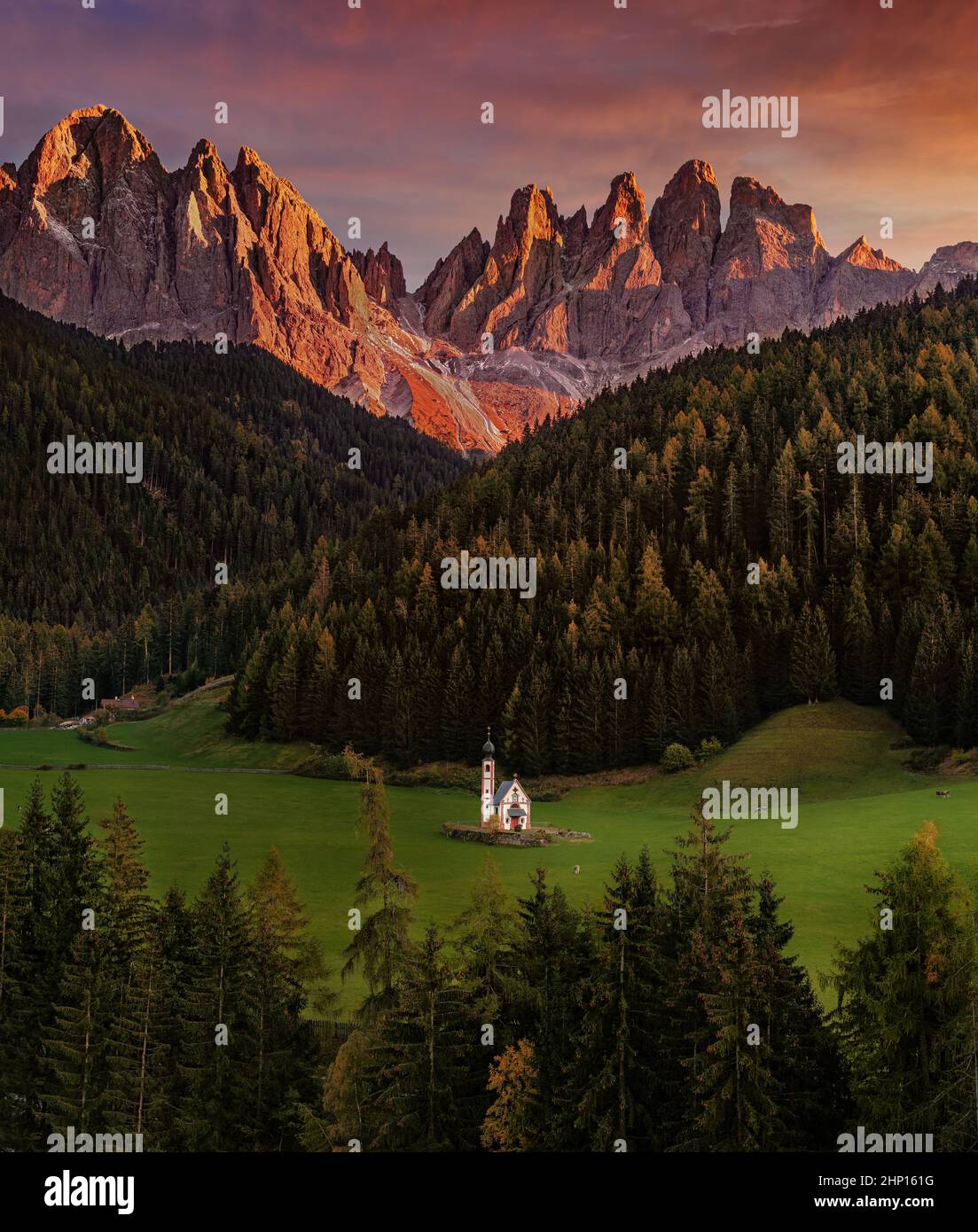 Val di Funes, Dolomiten, Italien - die wunderschöne St. Johann Kirche in Südtirol mit den italienischen Dolomiten und spektakulärem bunten Sonnenuntergang am Backgrou Stockfoto