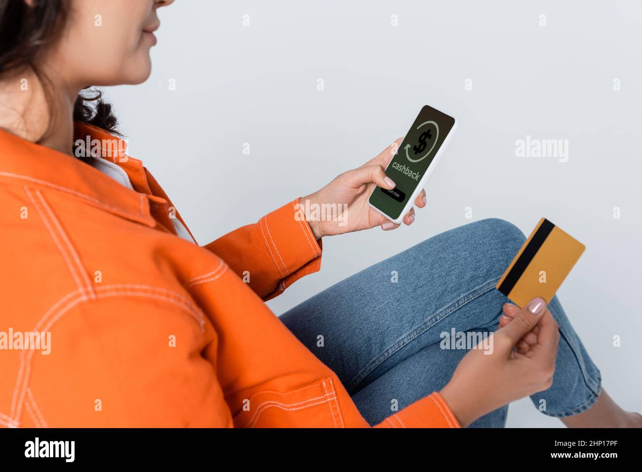 Beschnittene Ansicht einer Frau, die ein Smartphone mit Cashback auf dem Bildschirm verwendet und die Kreditkarte auf grau isoliert hält Stockfoto