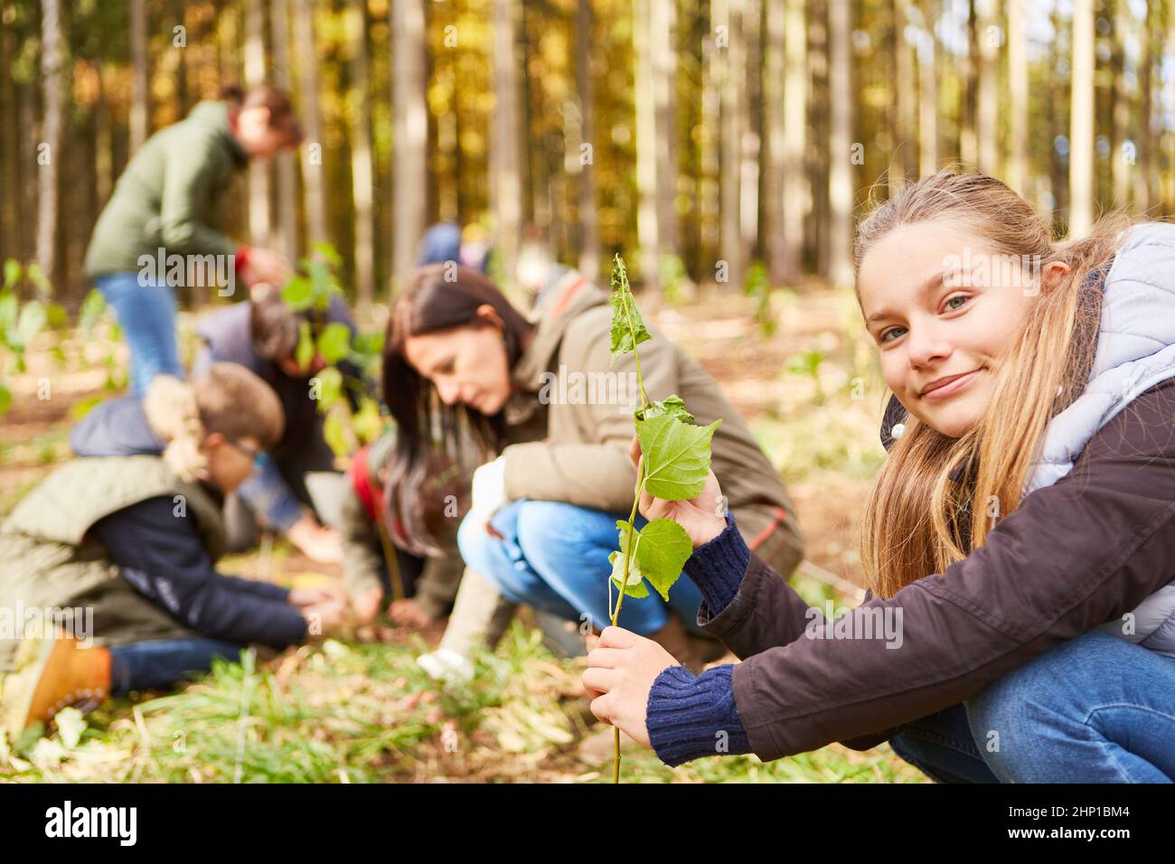 Mädchen pflanzt einen Baumkeimling als Baum des Klimawandels mit Familie im Hintergrund Stockfoto