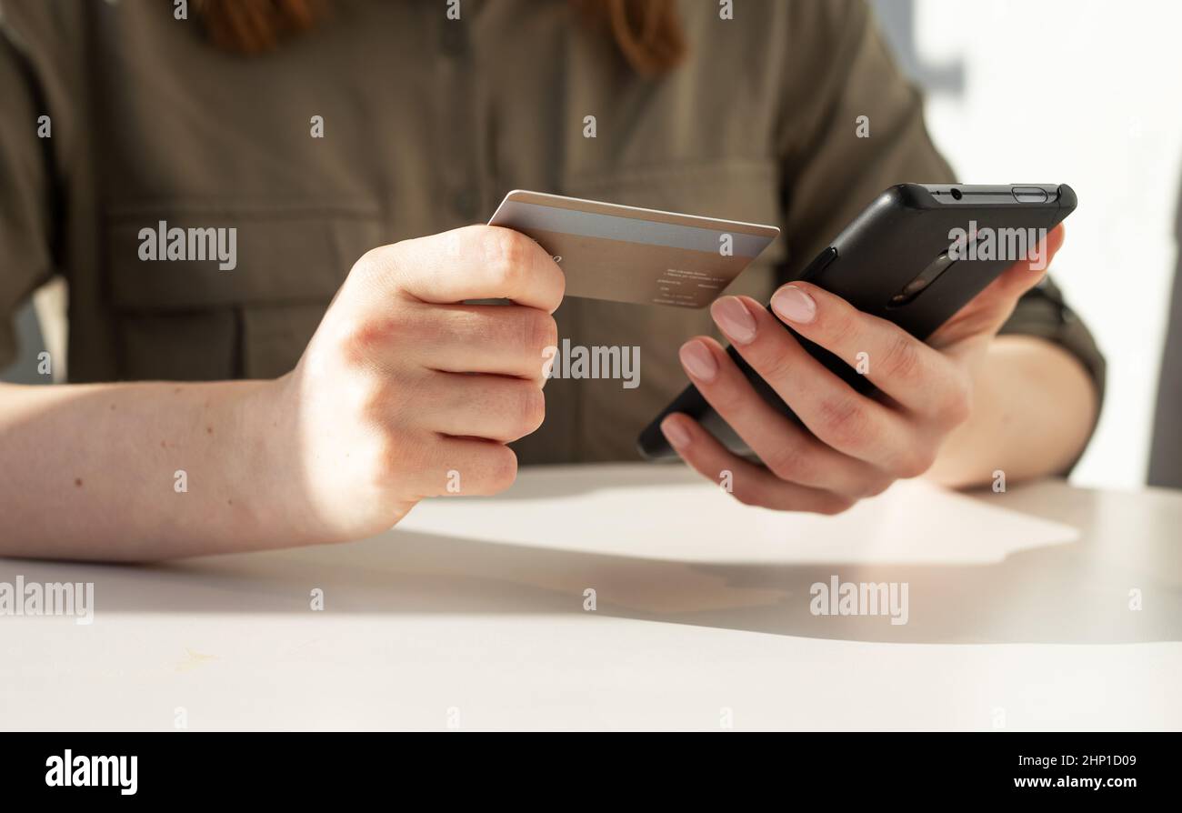 Frau Hände Nahaufnahme mit Kreditkarte und Telefon. Frau, die am Tisch sitzt und in der Anwendung bezahlt, online einkauft oder Bankgeschäfte macht. Hochwertige Fotos Stockfoto