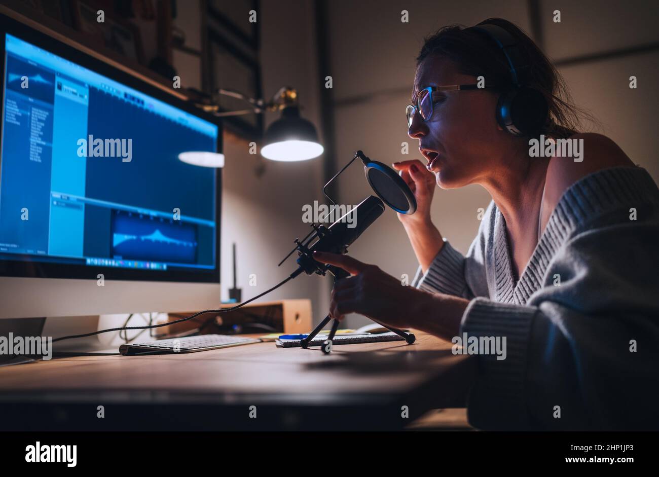 Junge Frau in Kopfhörern, die Stimmstimme mit Mikrofon mit POP-Filter und Desktop-Computer aufgenommen hat. Home Sound Studio Moderne Audio-Aufnahme techn Stockfoto