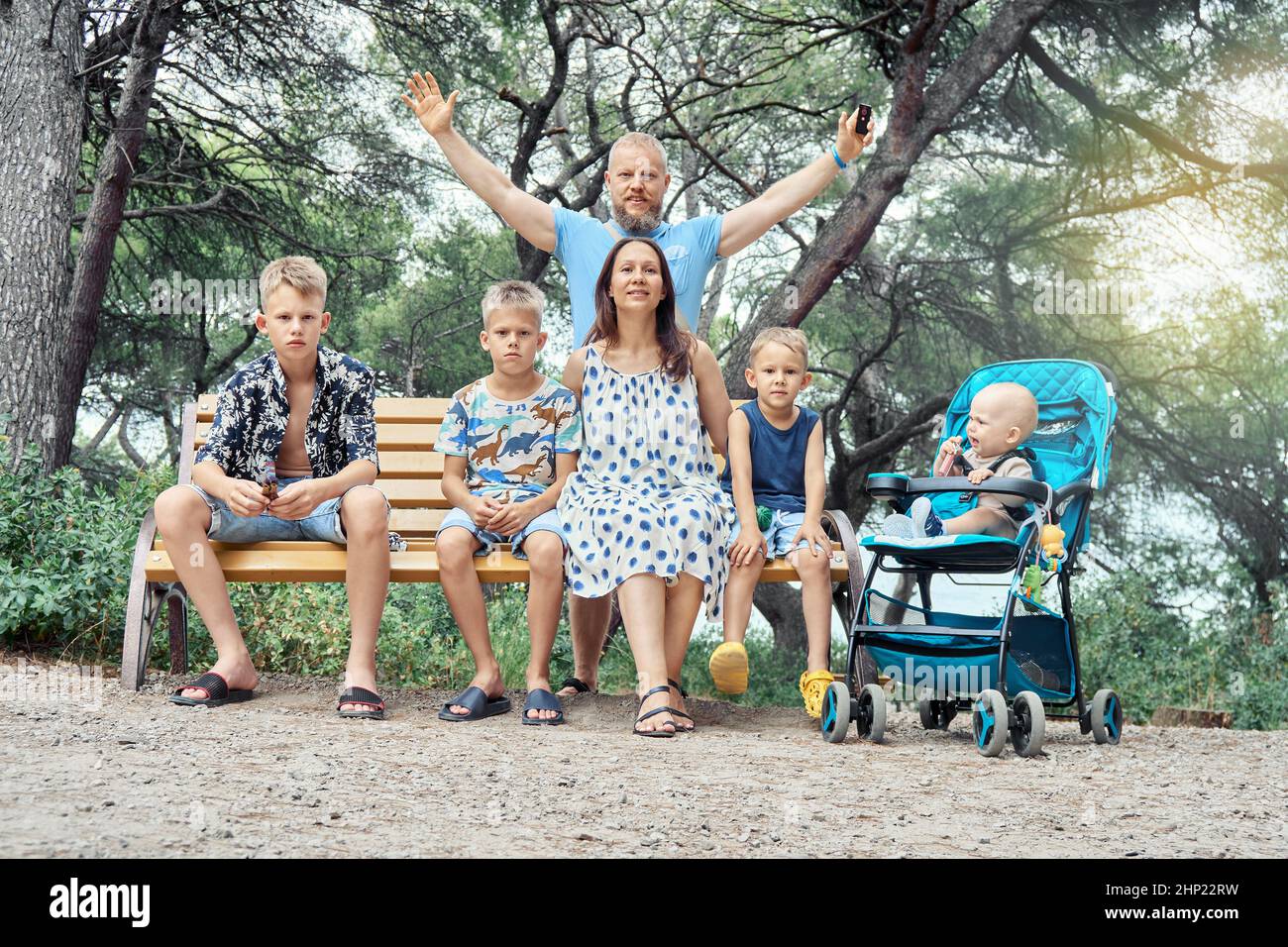 Glückliche große Familie posiert sitzen auf der Bank im grünen Park. Lächelnde Eltern und Söhne unterschiedlichen Alters genießen es, sich in der Natur gegen Bäume und Sträucher auszuruhen Stockfoto