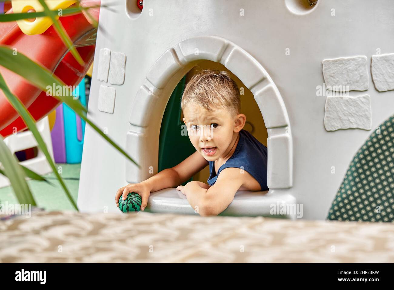 Lächelnder Junge spielt im Spielzeughaus im Unterhaltungsbereich des Restaurants mit Ball. Der blonde kleine Junge verbringt seine Freizeit damit, Nahaufnahme zu spielen Stockfoto