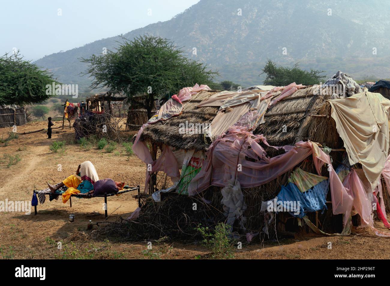 Verstörte Frau, die im Freien auf einem Kinderbett sitzt, nachdem sie durch einen Regensturm in ihrer Hütte in der Wüste Thar in der Nähe von Pushkar, Indien, beschädigt wurde. Stockfoto