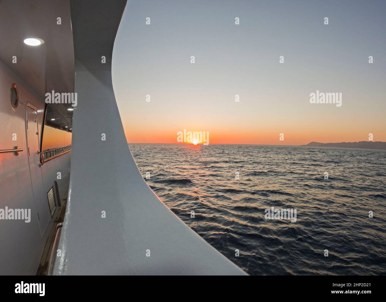 Blick von der Seite der großen Luxus-Motoryacht auf das Meer mit Blick auf den tropischen Ozean im Hintergrund und Sonnenaufgang am Horizont Stockfoto