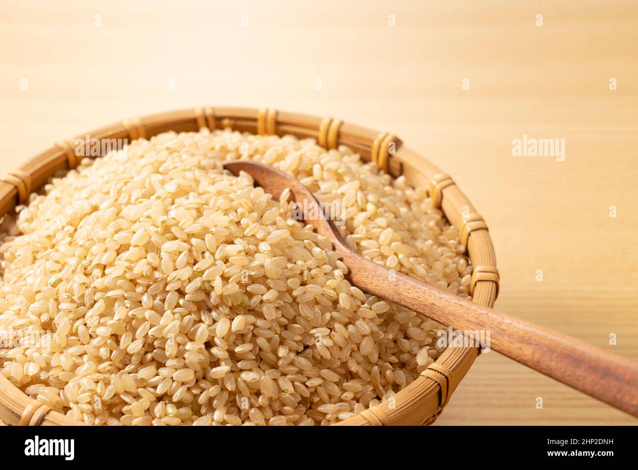 Brauner Reis in einem Bambuskolander und ein Holzlöffel auf einem hölzernen Hintergrund. Ein Haufen brauner Reis. Stockfoto