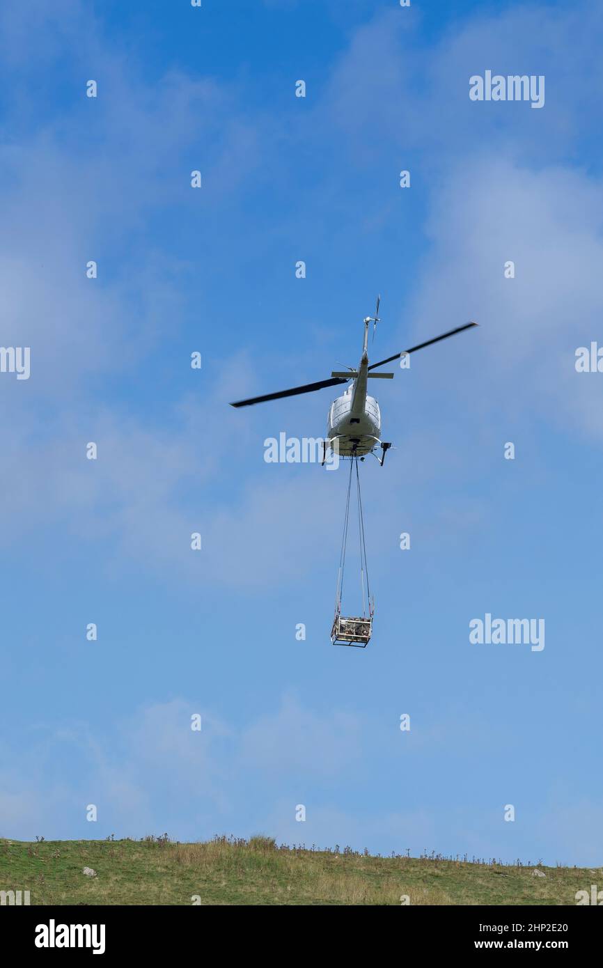 Hubschrauber, der eine Ladung Stein trägt, um auf das Moorland zu steigen, um bei der Wiederherstellung von Moor in den Yorkshire Dales, Großbritannien, zu helfen. Stockfoto