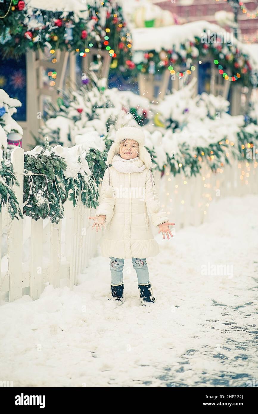 Ein lächelndes kleines Mädchen auf dem Wintermarkt. Trägt einen weißen Mantel. Stockfoto