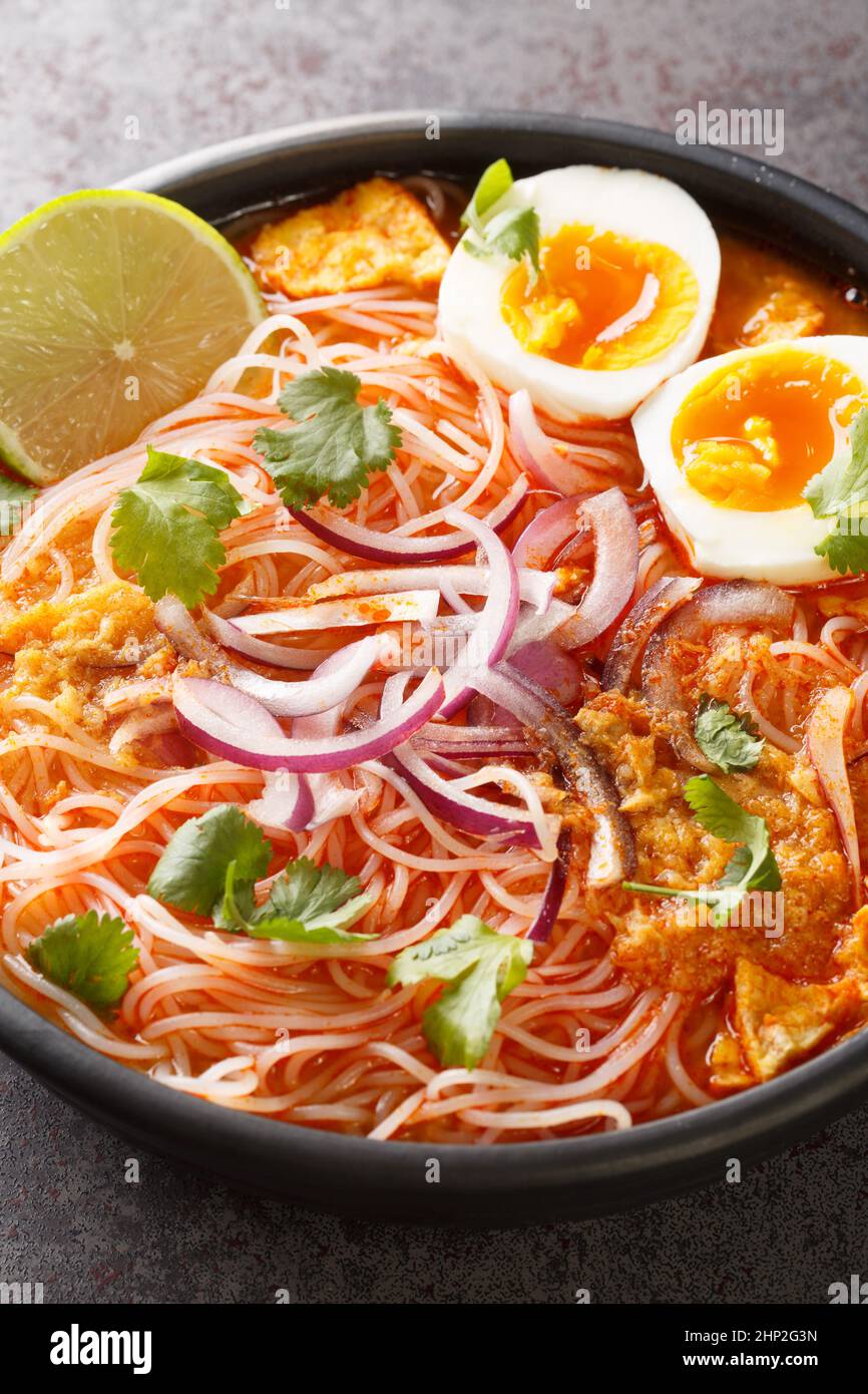 Burmesische traditionelle oder klassische Fischsuppe mit weißen flachen Nudeln namens Mohinga in der Schüssel auf dem Tisch. Vertikal Stockfoto