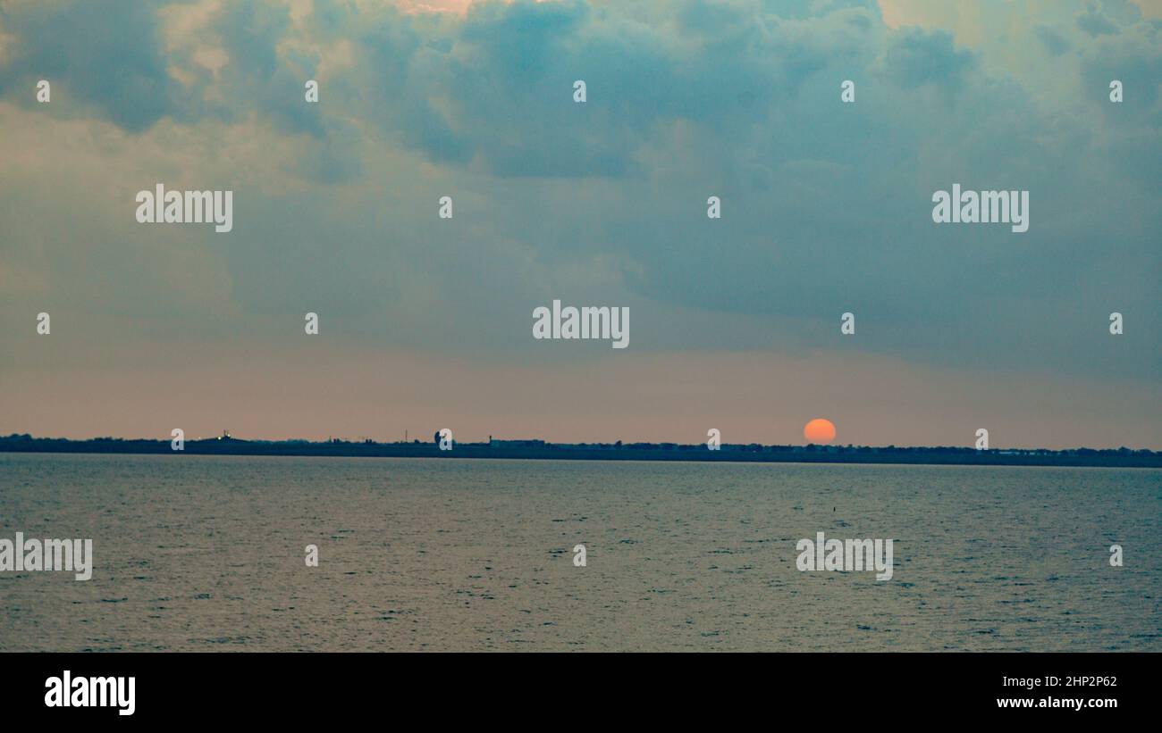 Wunderschöne Landschaft des Sonnenuntergangs am Strand. Ruhiges Wetter mit blauen Wolken am blauen Himmel, die sich im Wasser spiegeln. Stockfoto