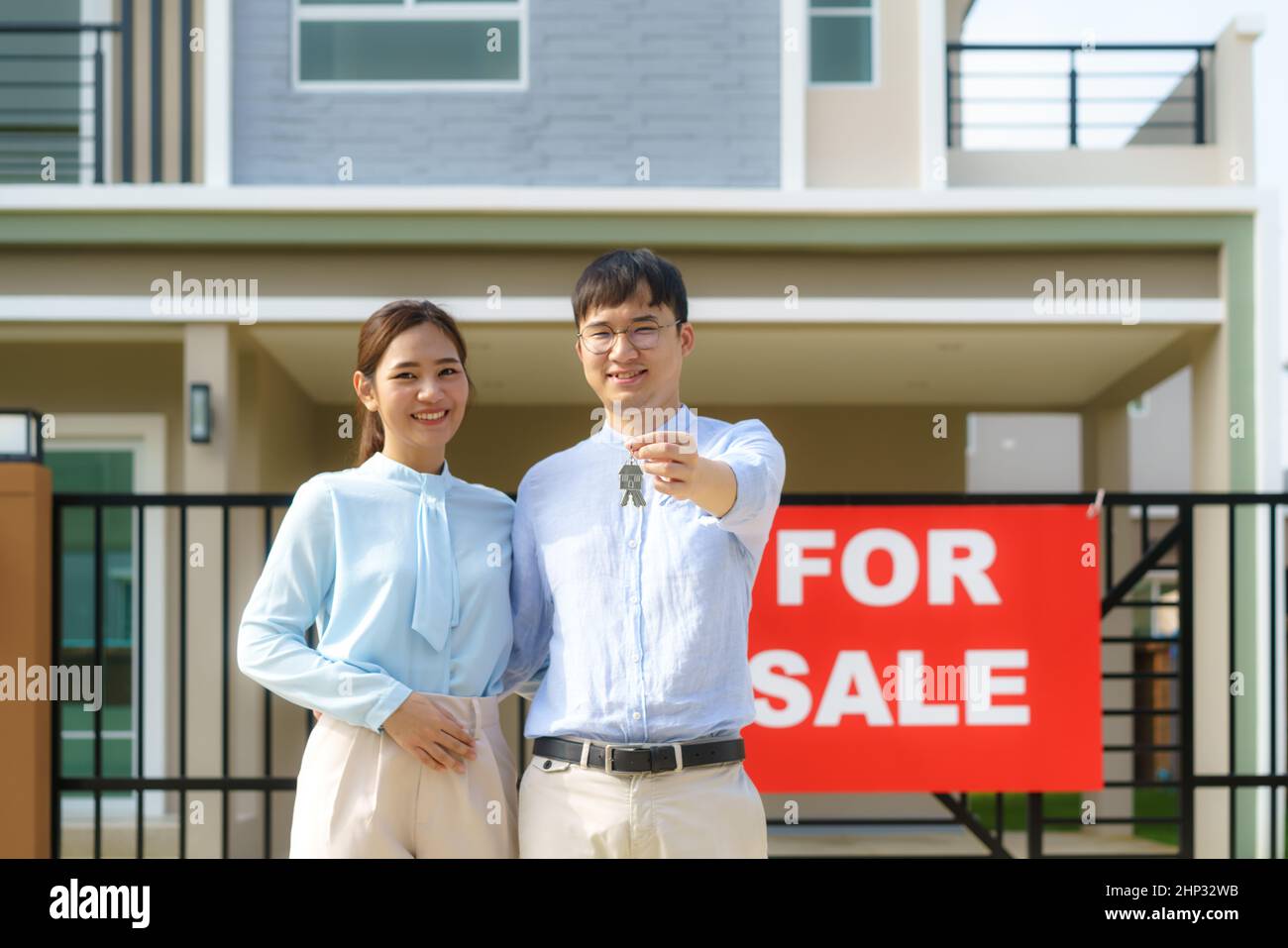 Porträt des jungen asiatischen Paares, das zusammen steht und umarmt und die Haustaste hält, die vor ihrem neuen Haus glücklich aussieht, um neues Leben zu beginnen. Familie Stockfoto
