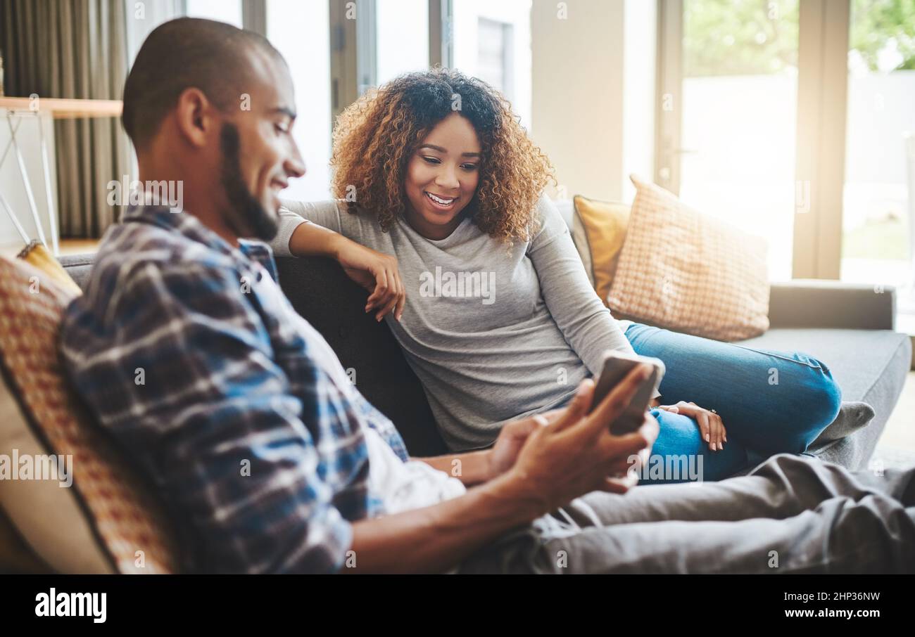Die gesunde Ehe hält die Kommunikationswege offen. Aufnahme eines jungen Paares, das sich zu Hause auf dem Sofa entspannt und zusammen ein Mobiltelefon benutzt. Stockfoto