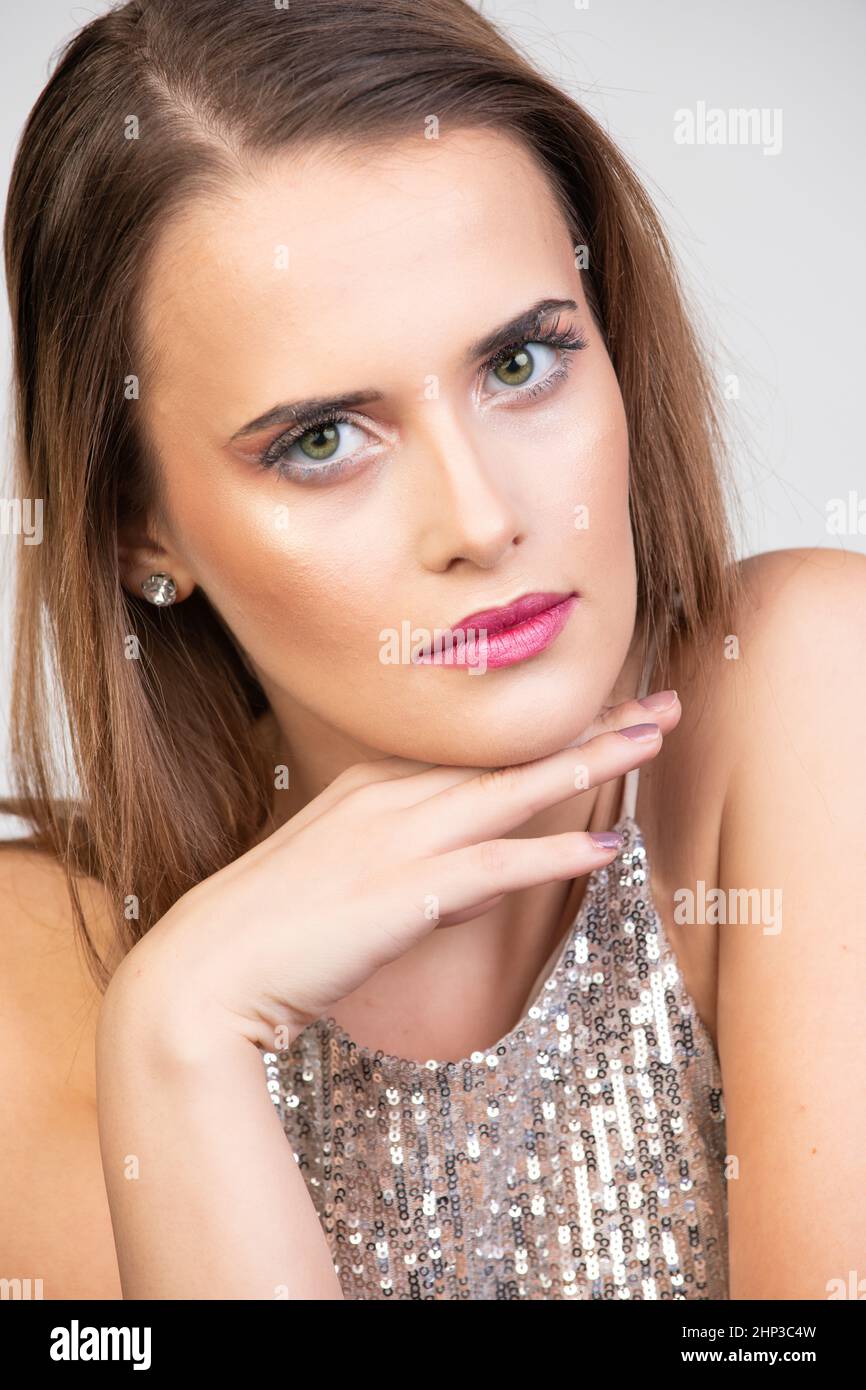 Eine junge, hübsche Frau mit langen, geraden Brünetten Haaren propft ihr Kinn auf einer Hand. Stockfoto