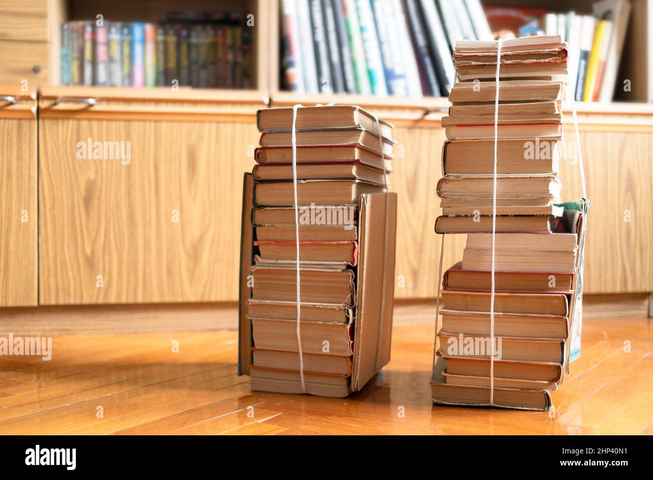 Zwei Stapel gebrauchter Bücher, die mit Verpackungsfaden auf Parkettboden im Wohnzimmer neben dem Bibliotheksschrank gebunden sind Stockfoto