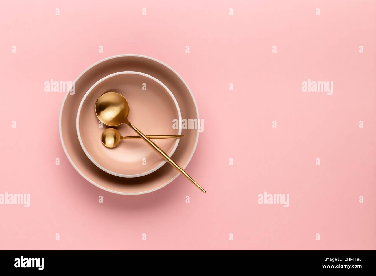 Zwei Suppenschüsseln und Löffel auf einem rosafarbenen Tisch, Draufsicht. Goldenes Besteck zum Servieren und Essen. Set aus beigefarbenen runden Tellern. Vorlage mit Kopierplatz für te Stockfoto