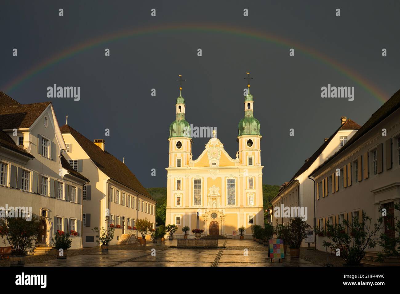 Arlesheimer Dom nach einem Gewitter. Der Himmel ist dunkel mit einem Regenbogen direkt über der Kuppel, die Abendsonne erleuchtet die Kathedrale. Arlesheim Stockfoto