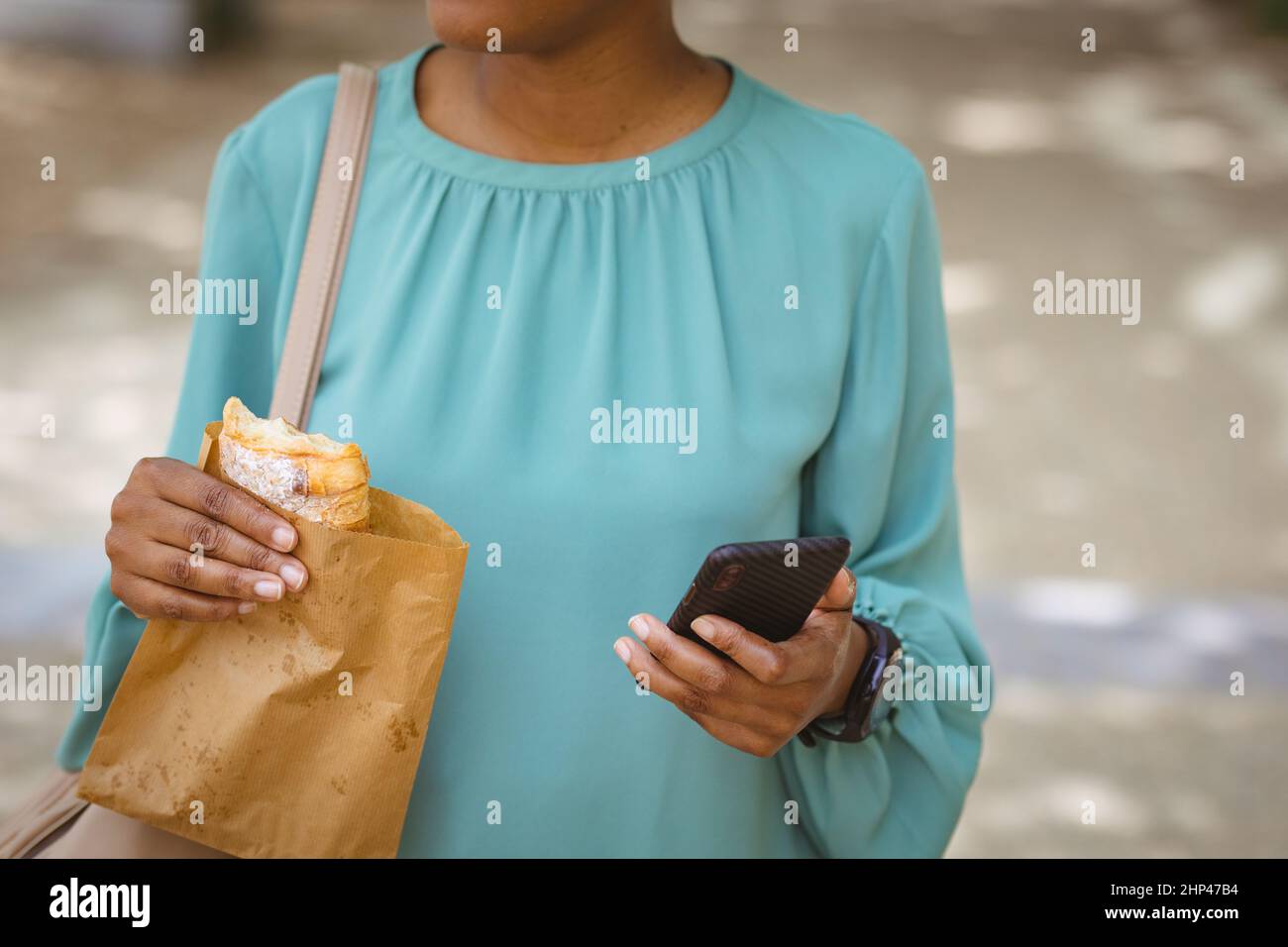 Mittelteil der Geschäftsfrau mit Smartphone und nehmen Sie Essen aus dem Park stehen Stockfoto