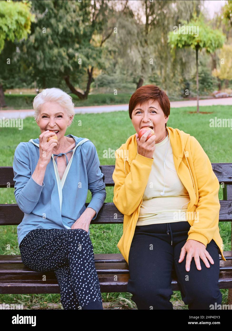 Zwei reife Frauen essen Äpfel auf der Bank nach dem Sport-Übungen im Park. Gesundes Lifestyle-Konzept Stockfoto
