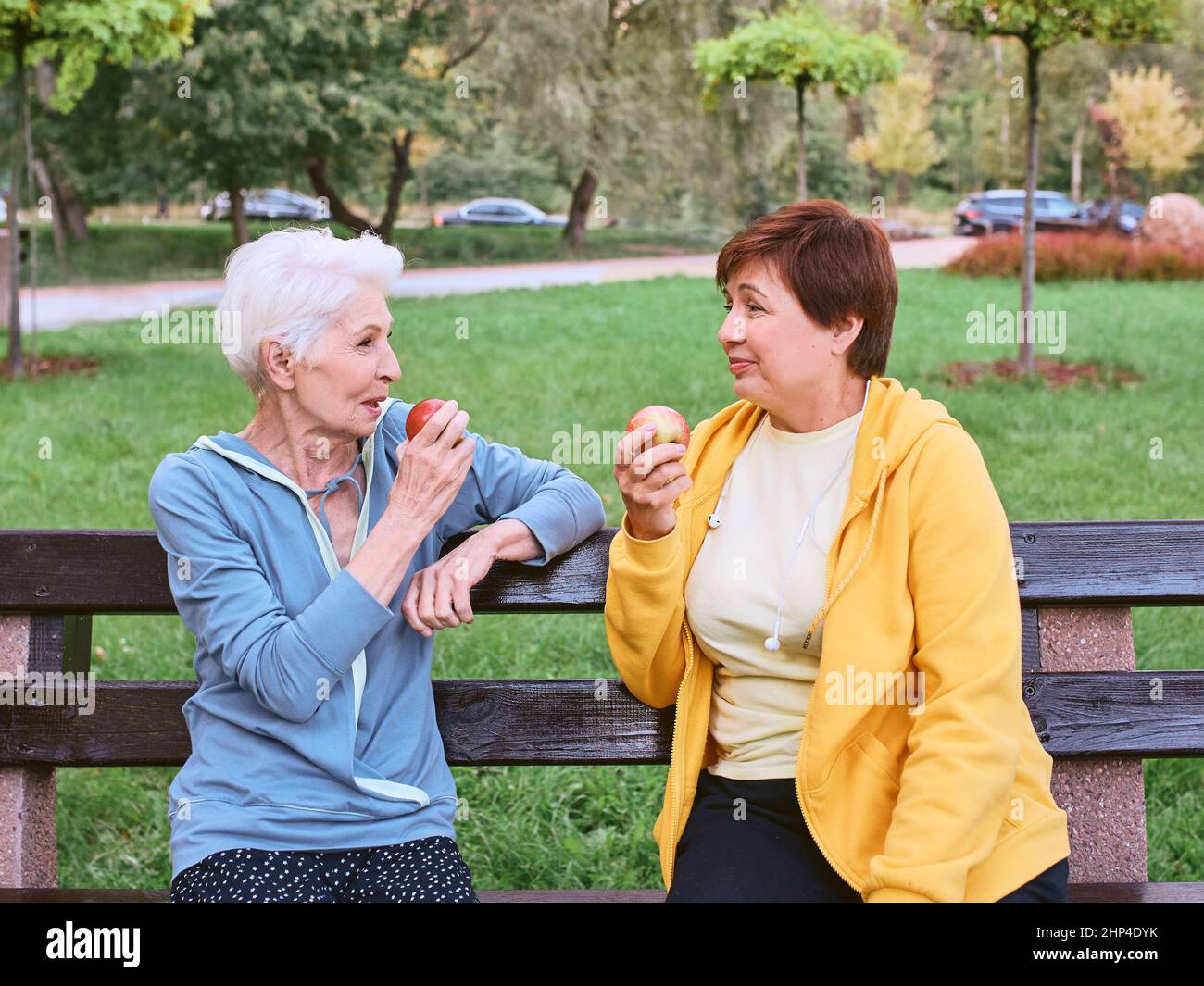 Zwei reife Frauen essen Äpfel auf der Bank nach dem Sport-Übungen im Park. Gesundes Lifestyle-Konzept Stockfoto