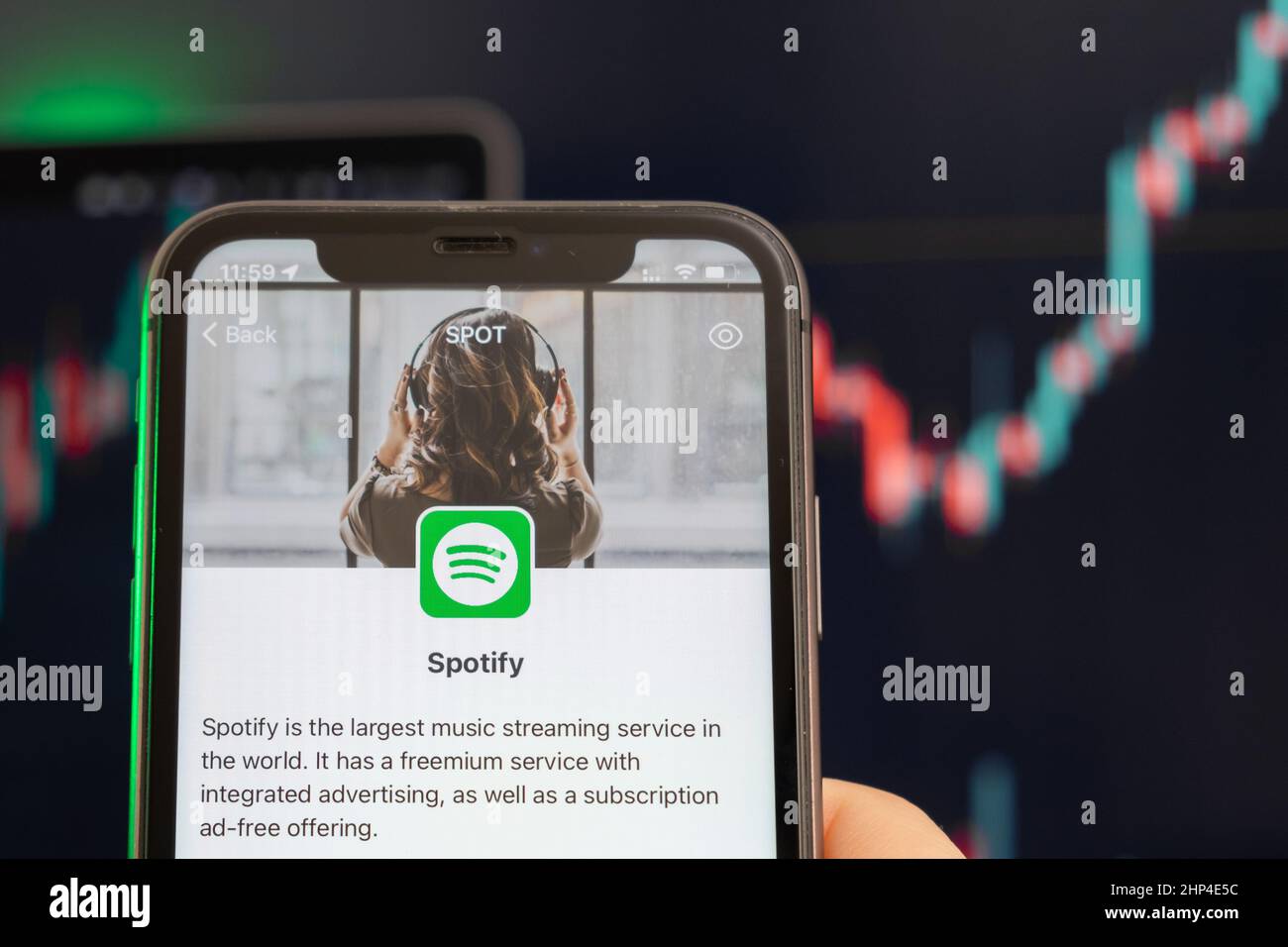 Aufwärtstrend bei den Spotify-Aktienkursen mit Grafiken im Hintergrund. Man hands Holding a Smartphone with Logo on the screen, February 2022, San Francisco, USA. Stockfoto
