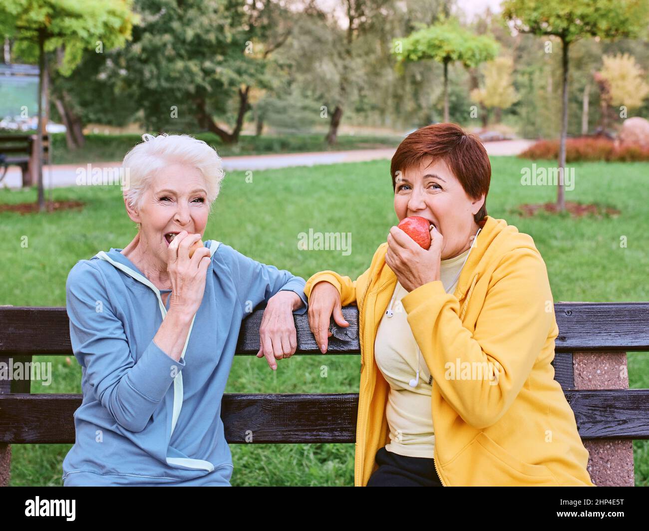 Zwei reife Frauen essen Äpfel auf der Bank nach dem Sport-Übungen im Park. Gesundes Lifestyle-Konzept Stockfoto