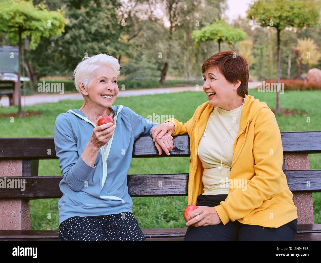 Zwei reife Frauen essen Äpfel auf der Bank nach dem Sport-Übungen im Park. Gesundes Lifestyle-Konzept Stockfoto