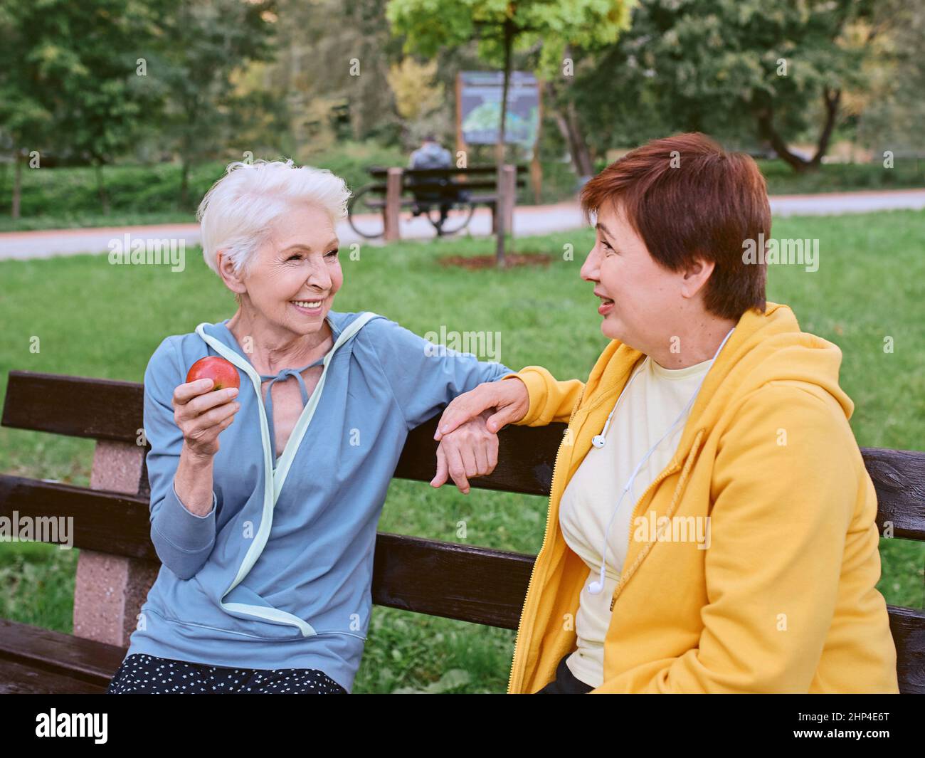 Zwei reife Frauen essen Äpfel auf der Bank nach dem Sport-Übungen im Park. Gesundes Lifestyle-Konzept Stockfoto