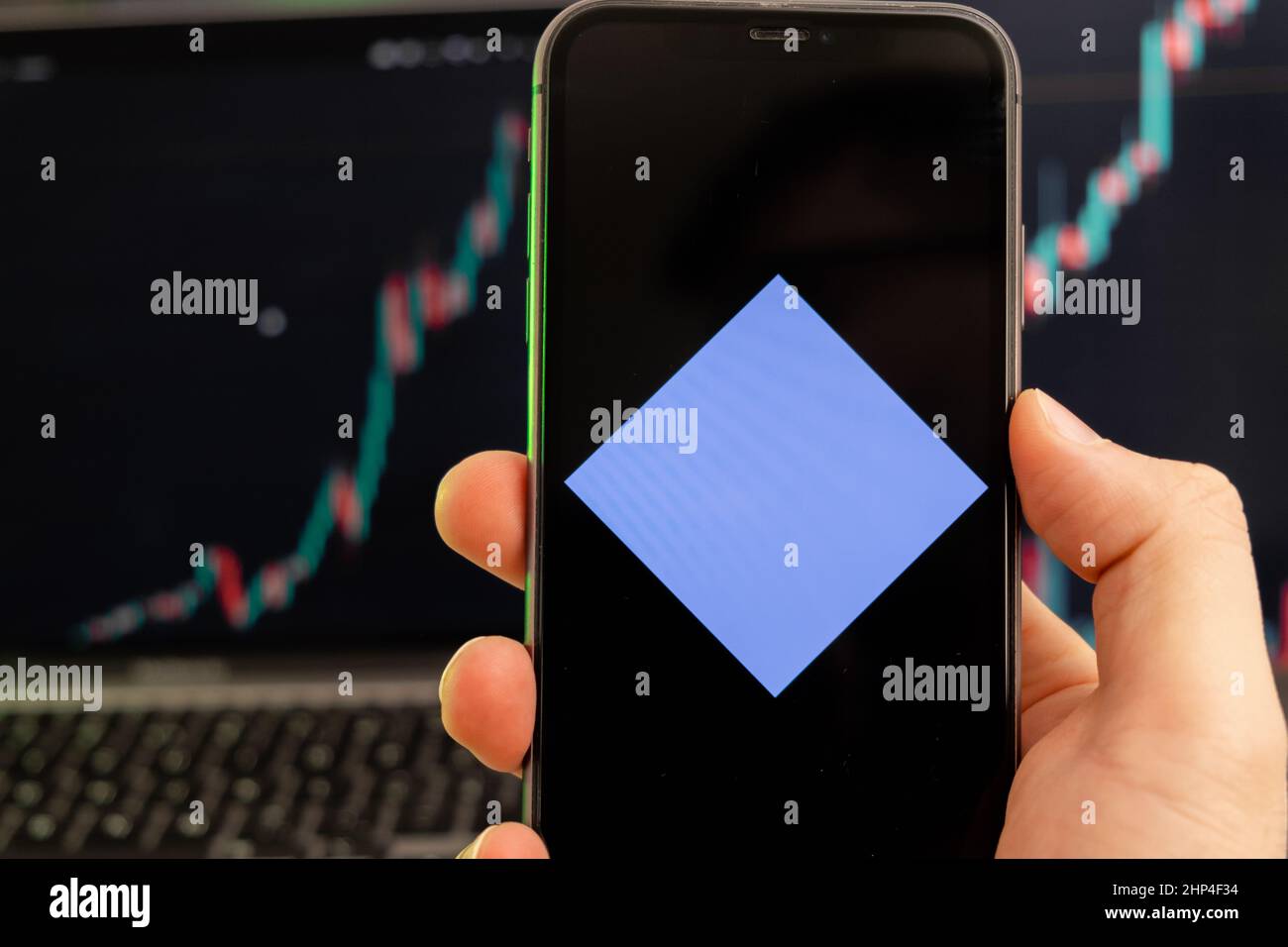 Wellen Kryptowährung Logo auf dem Bildschirm eines Smartphones in mans Hand mit einem wachsenden Trend auf dem Chart auf einem grünen Hintergrund. Stockfoto
