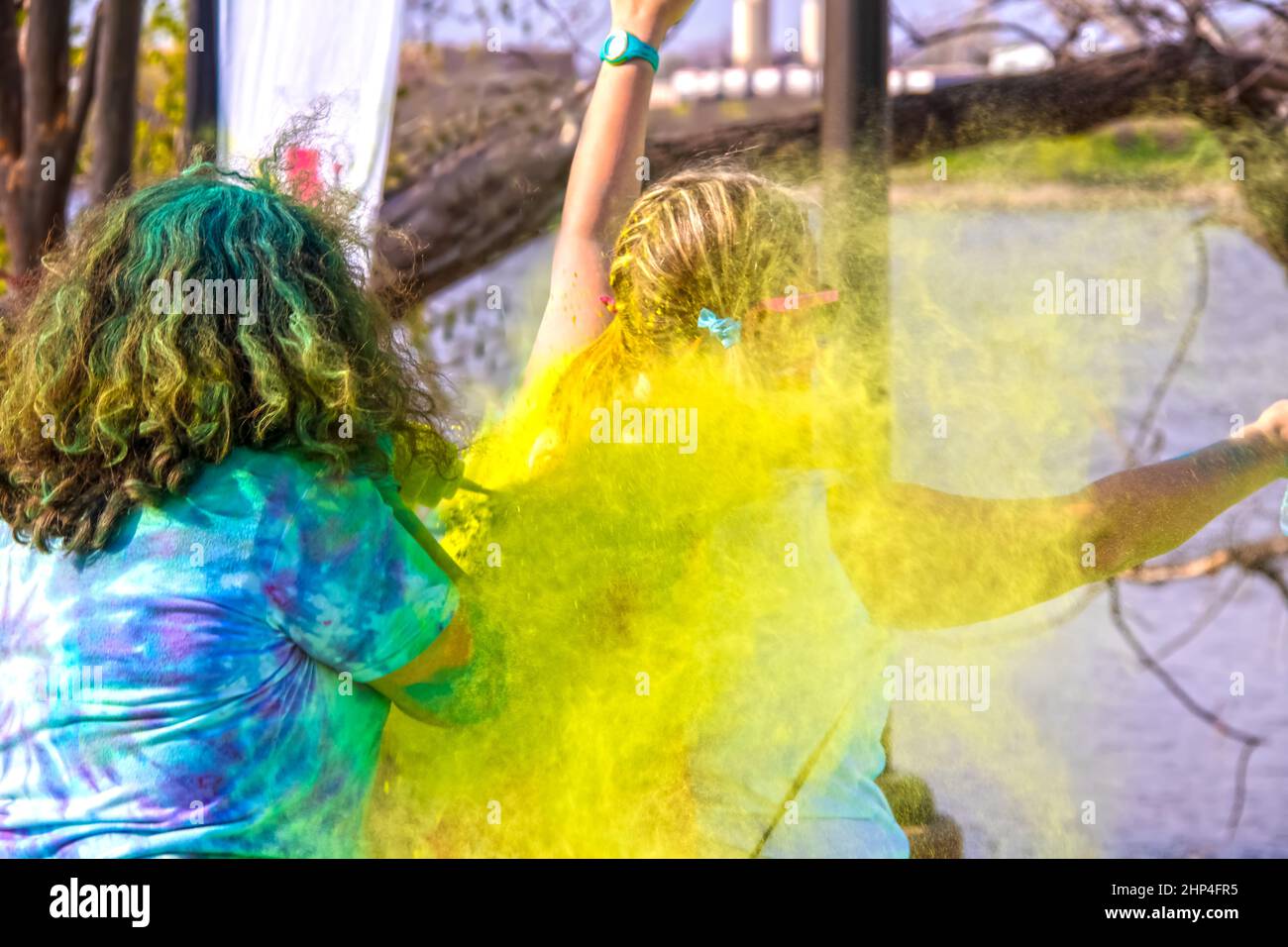 Mädchen mit aufgeweckten Armen wird beim Holi Color Festival mit gelbem Pulver überzogen - selektiver Fokus - unkenntliche Menschen - helle Farben Stockfoto