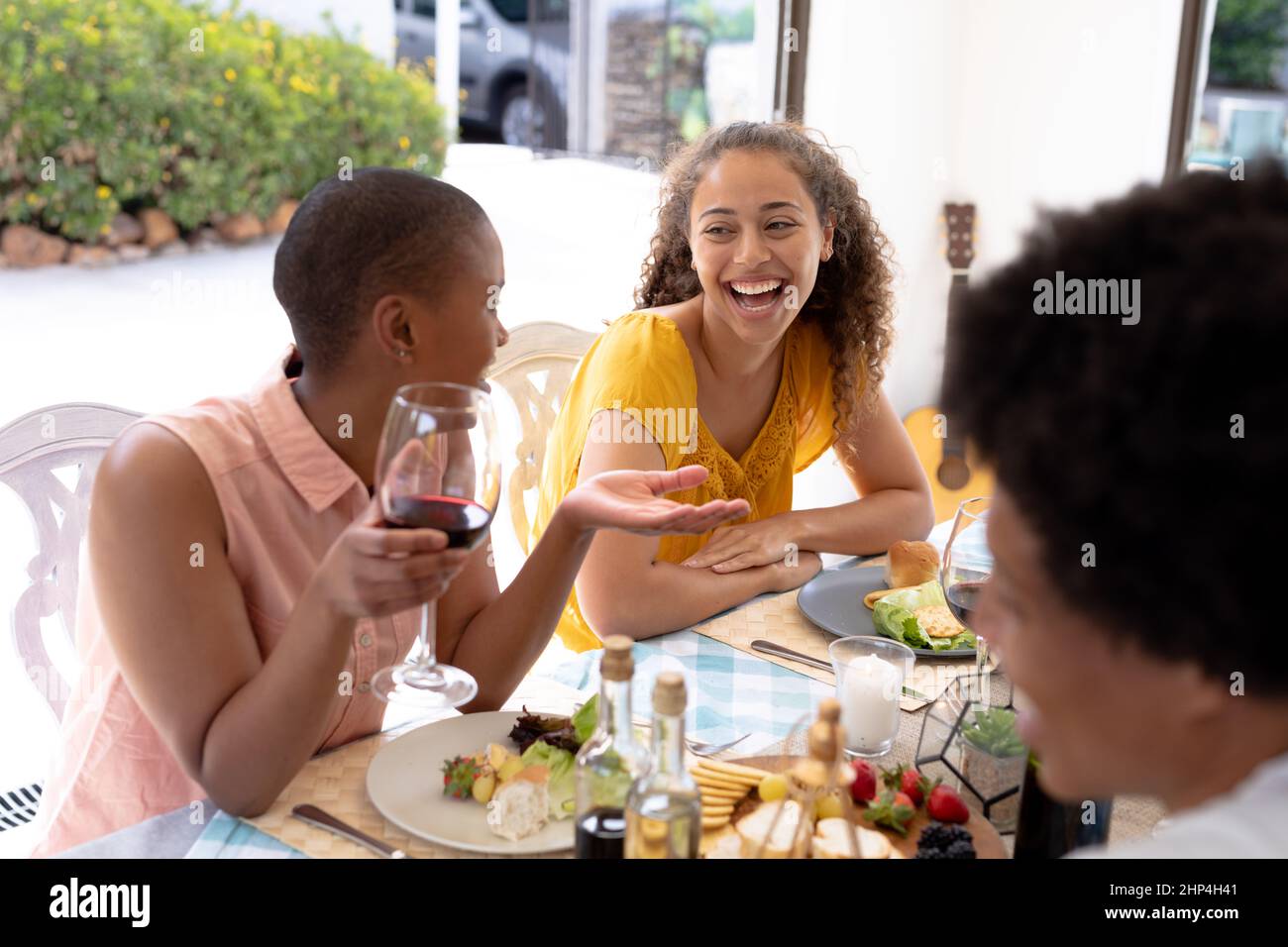 Fröhliche junge weibliche multirassische Freunde lachen zusammen, während sie am Esstisch sitzen Stockfoto