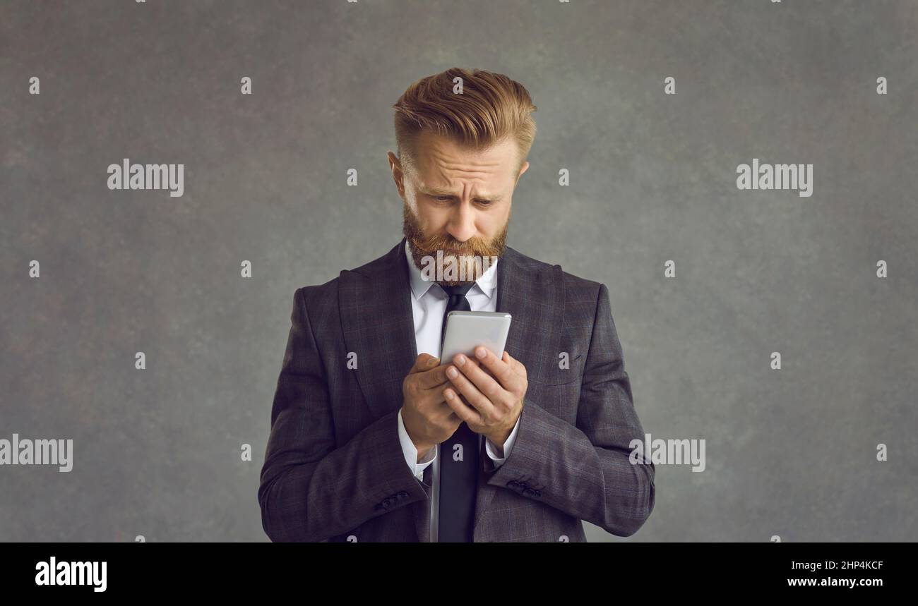Unglücklicher Geschäftsmann isoliert auf grauem Hintergrund mit Problem mit dem Mobiltelefon Stockfoto