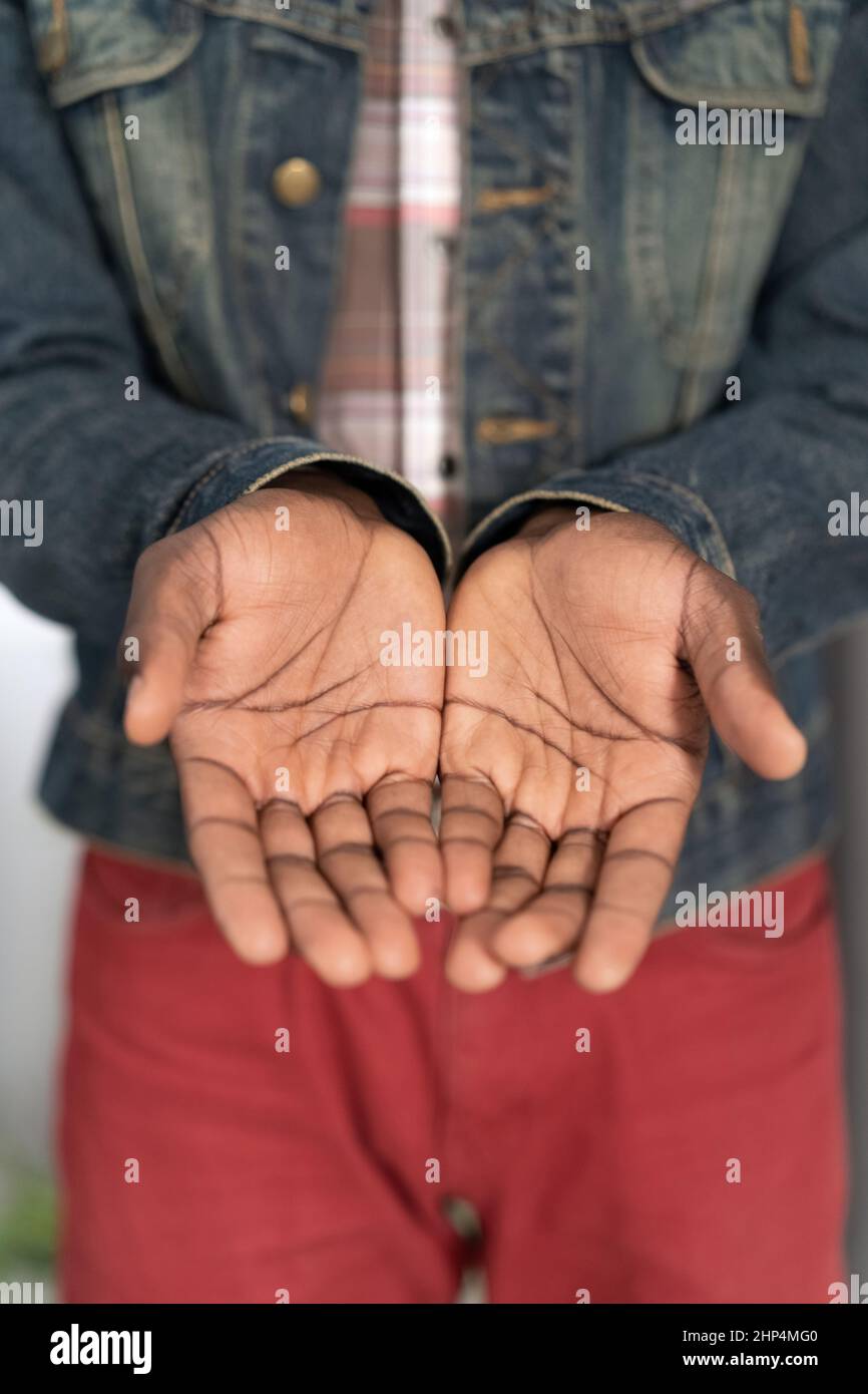 Bettelhände eines armen Mannes Konzept. Öffnen Sie die Hände eines jungen afroamerikanischen Mannes, der eine Jeansjacke trägt. Junger afroamerikanischer Mann mit ausgestreckten Händen bettelt um Geld für das Leben. Stockfoto
