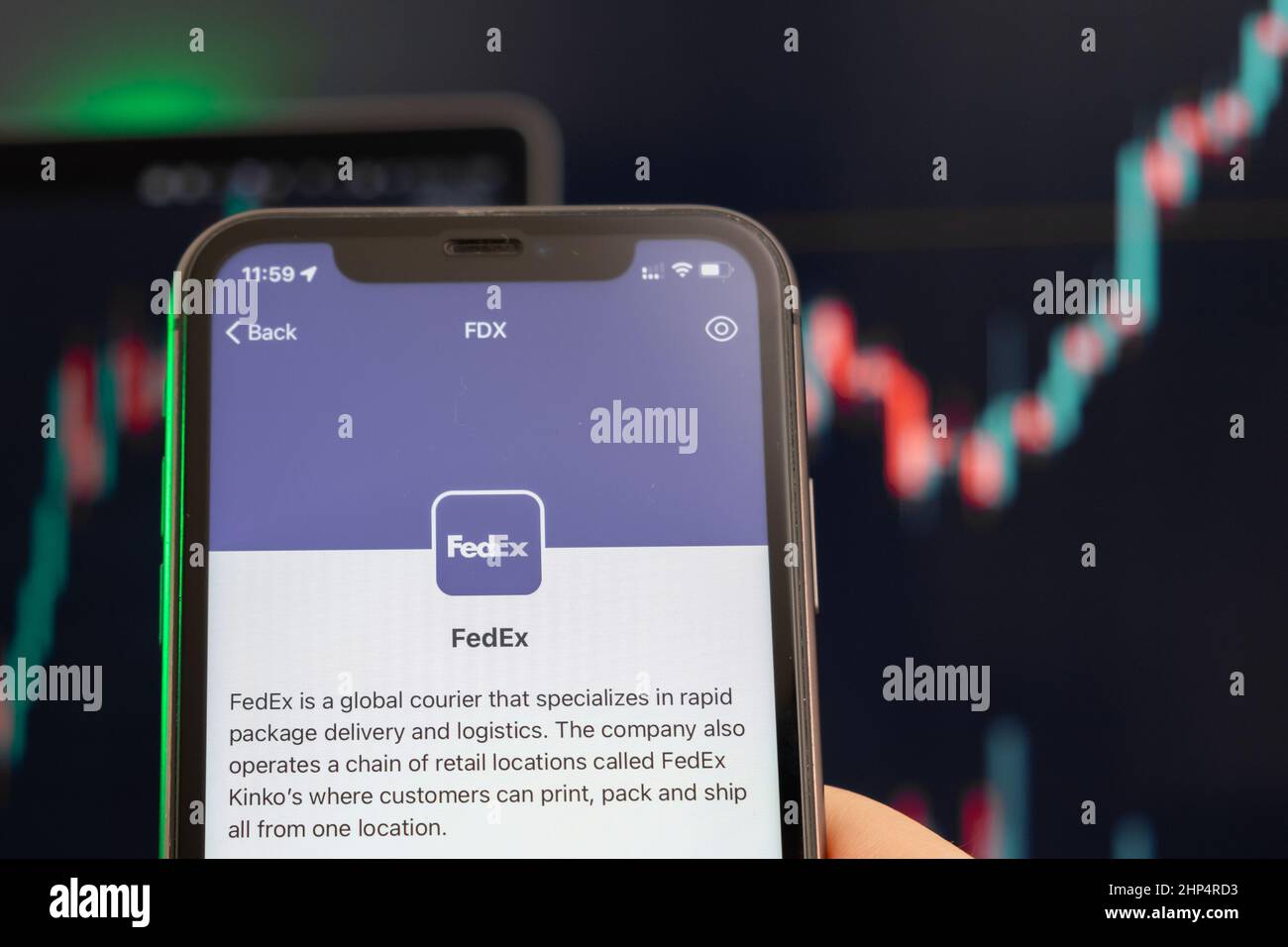 Der Aufwärtstrend der FedEx-Aktienkursen mit Grafiken im Hintergrund. Man hands Holding a Smartphone with Logo on the screen, February 2022, San Francisco, USA. Stockfoto