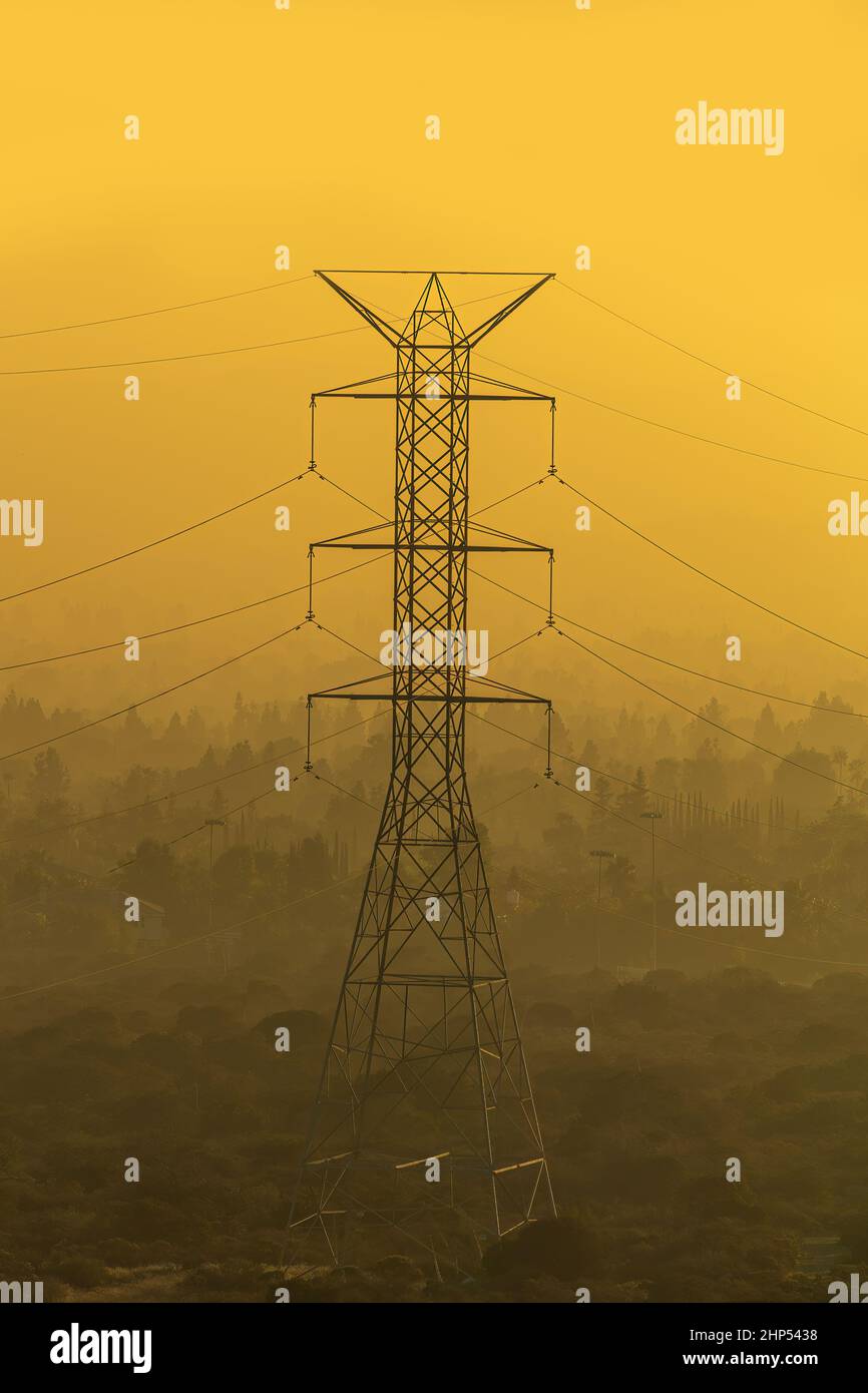 Die Energiekrise auf einen Blick: Ein massiver Stahlleitungsübertragungsturm in goldenem, dunstigen Nebel. Stockfoto