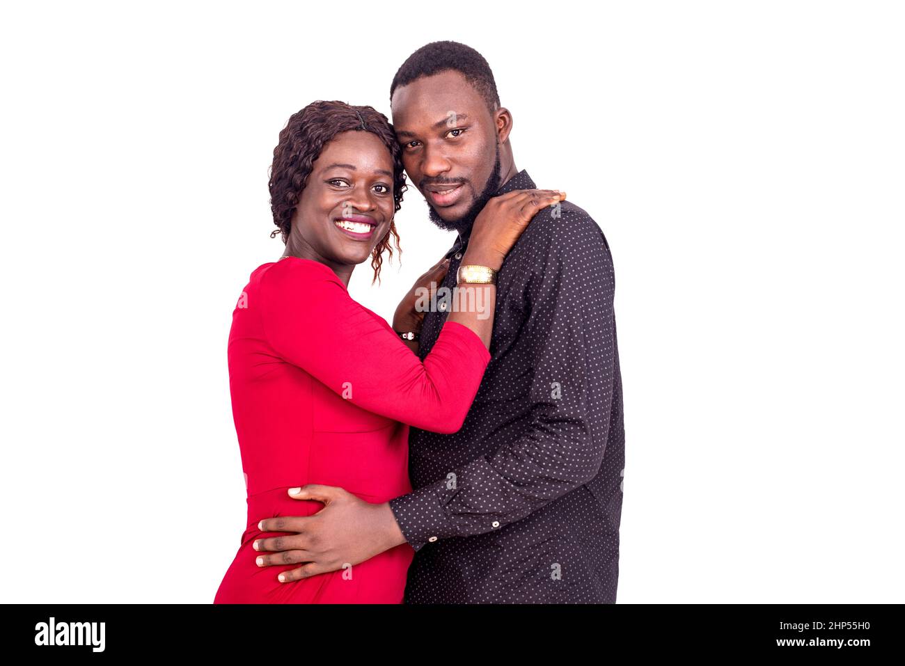 Junges afrikanisches Paar, das auf weißem Hintergrund stand, verschlungte sich und schaute lächelnd auf die Kamera. Stockfoto