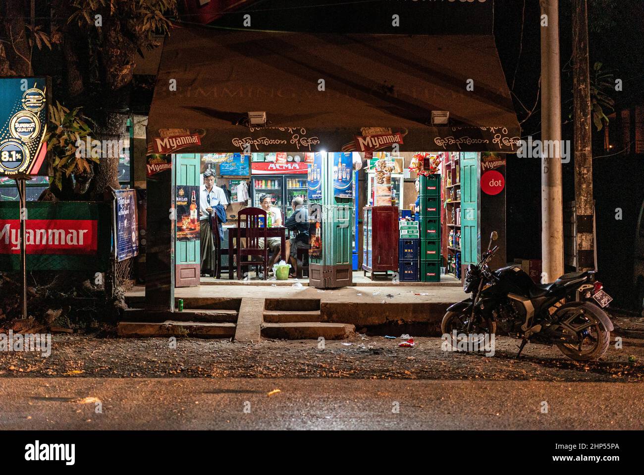 Wunderschöne Aufnahme eines Motorrads, das vor einem Laden geparkt wurde, wo zwei Leute nachts unterhielten Stockfoto