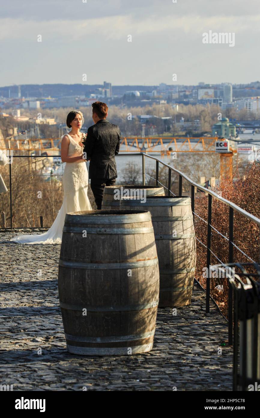 Ein japanisches Paar mit Braut in ihrem Hochzeitskleid auf einem Weinberg mit Blick auf die Moldau, mit Weinfässern im Vordergrund, Prag, Tschechische Republik Stockfoto