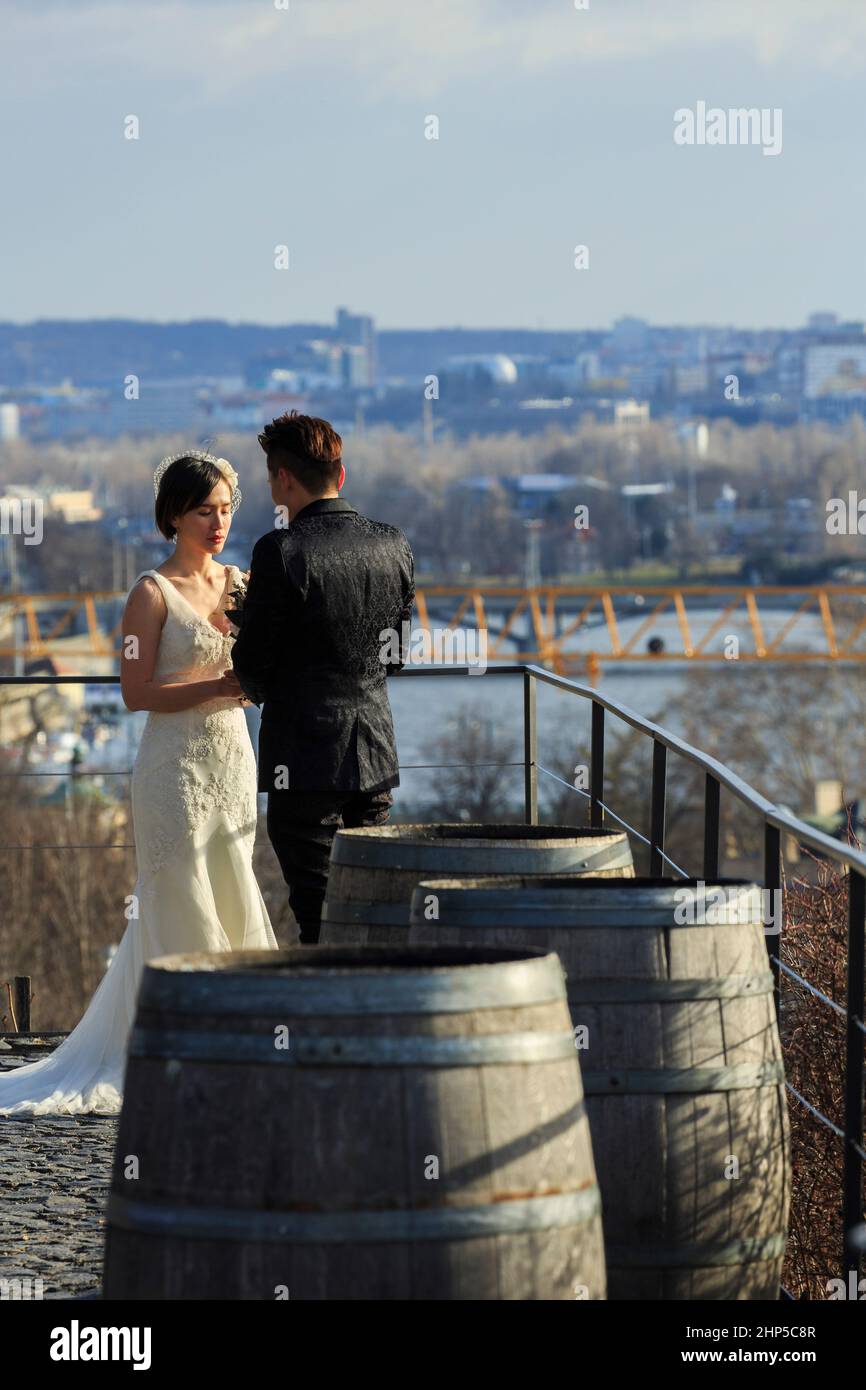 Ein japanisches Paar mit Braut in ihrem Hochzeitskleid auf einem Weinberg mit Blick auf die Moldau, mit Weinfässern im Vordergrund, Prag, Tschechische Republik Stockfoto