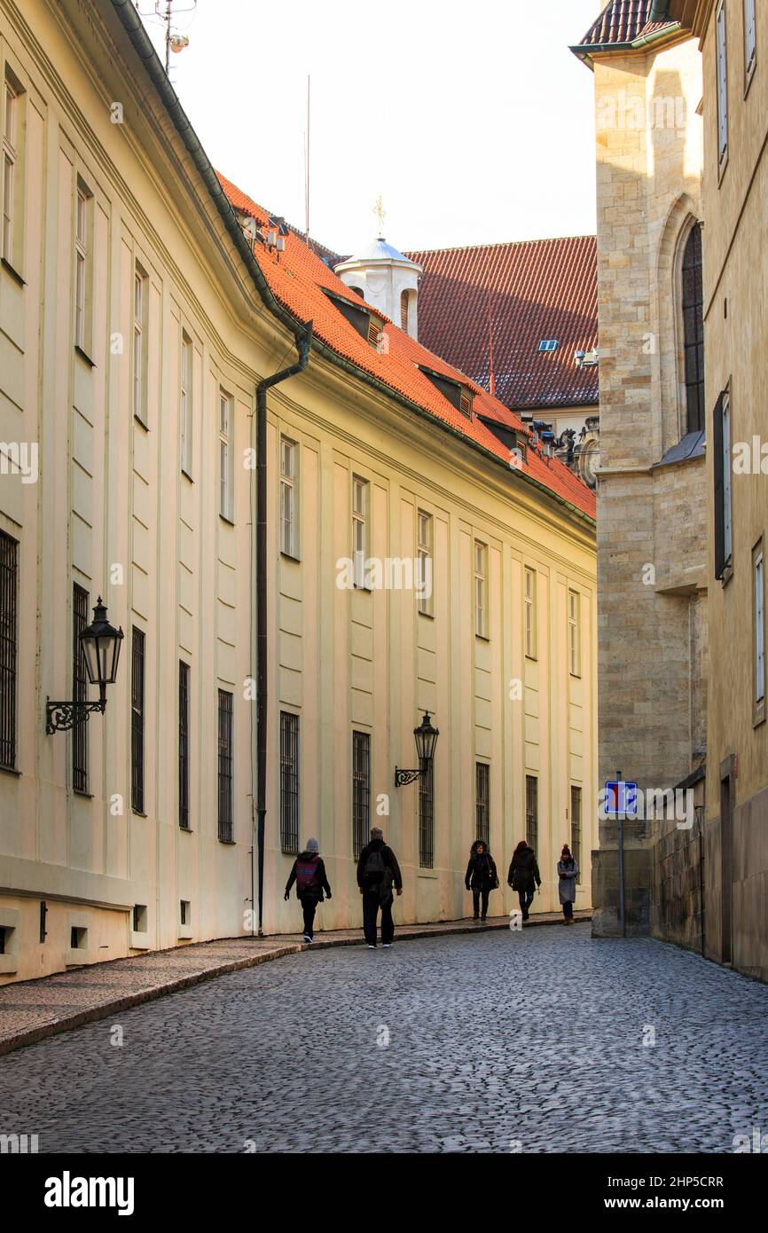 Morgenschatten in einer engen gepflasterten Straße in der Prager Burg mit klassischen Gebäuden und traditionellen Laternen Straßenbeleuchtung, mit Touristen, Prag Stockfoto