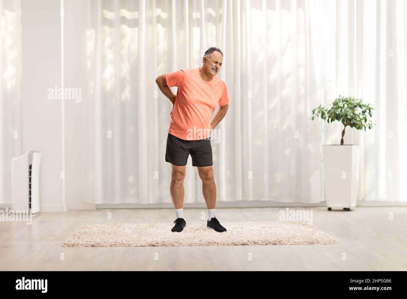 In voller Länge Porträt eines reifen Mannes in Sportkleidung, der seine Wirbelsäule zu Hause hält Stockfoto