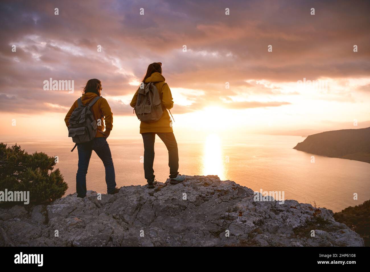 Zwei Wanderer mit Rucksäcken blicken vom Aussichtspunkt aus auf den Sonnenuntergang Stockfoto