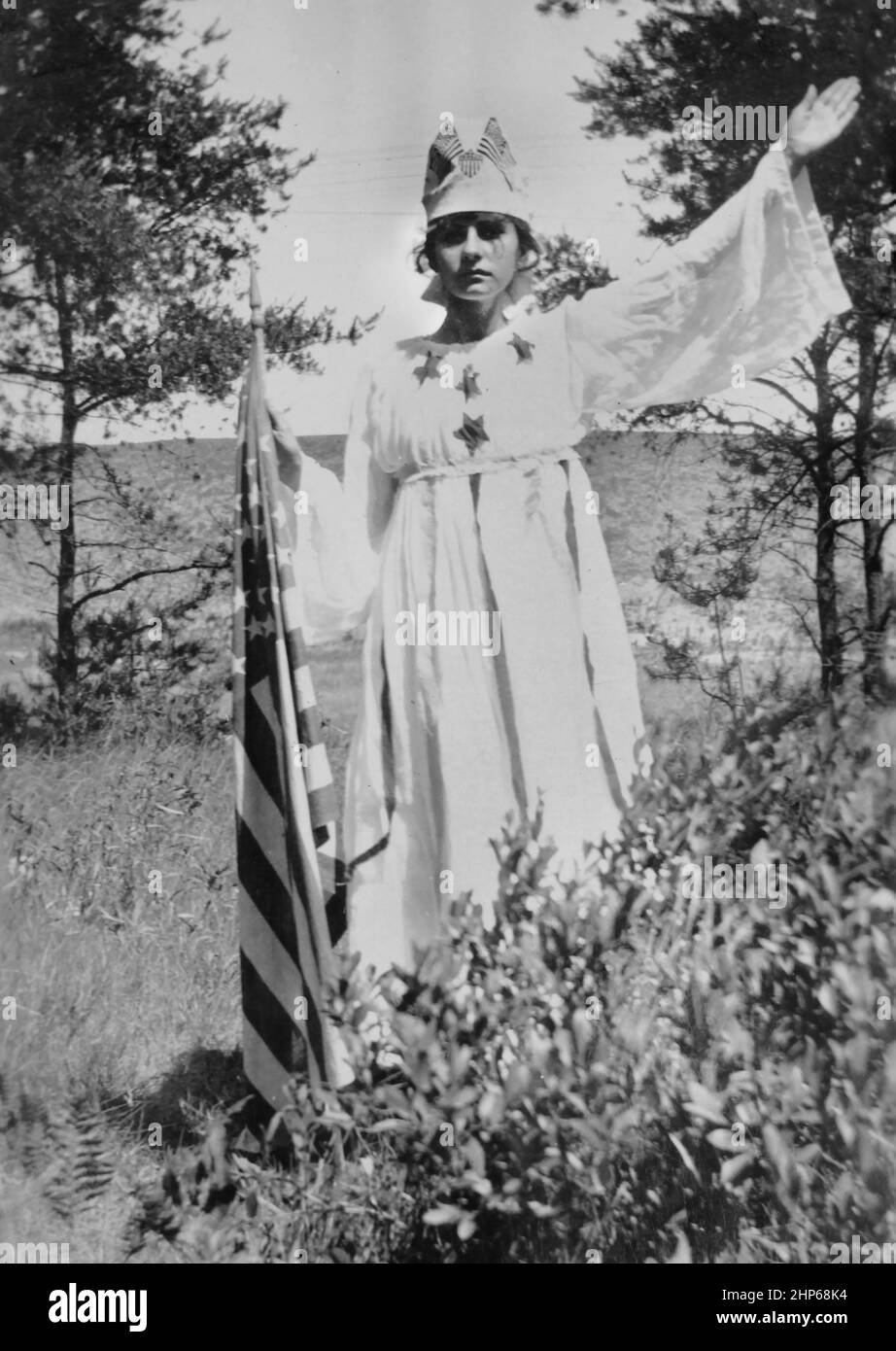 Ein Teenager posiert draußen in ihrem patriotischen Kostüm, während er eine amerikanische Flagge hält, ca. 1910. Stockfoto