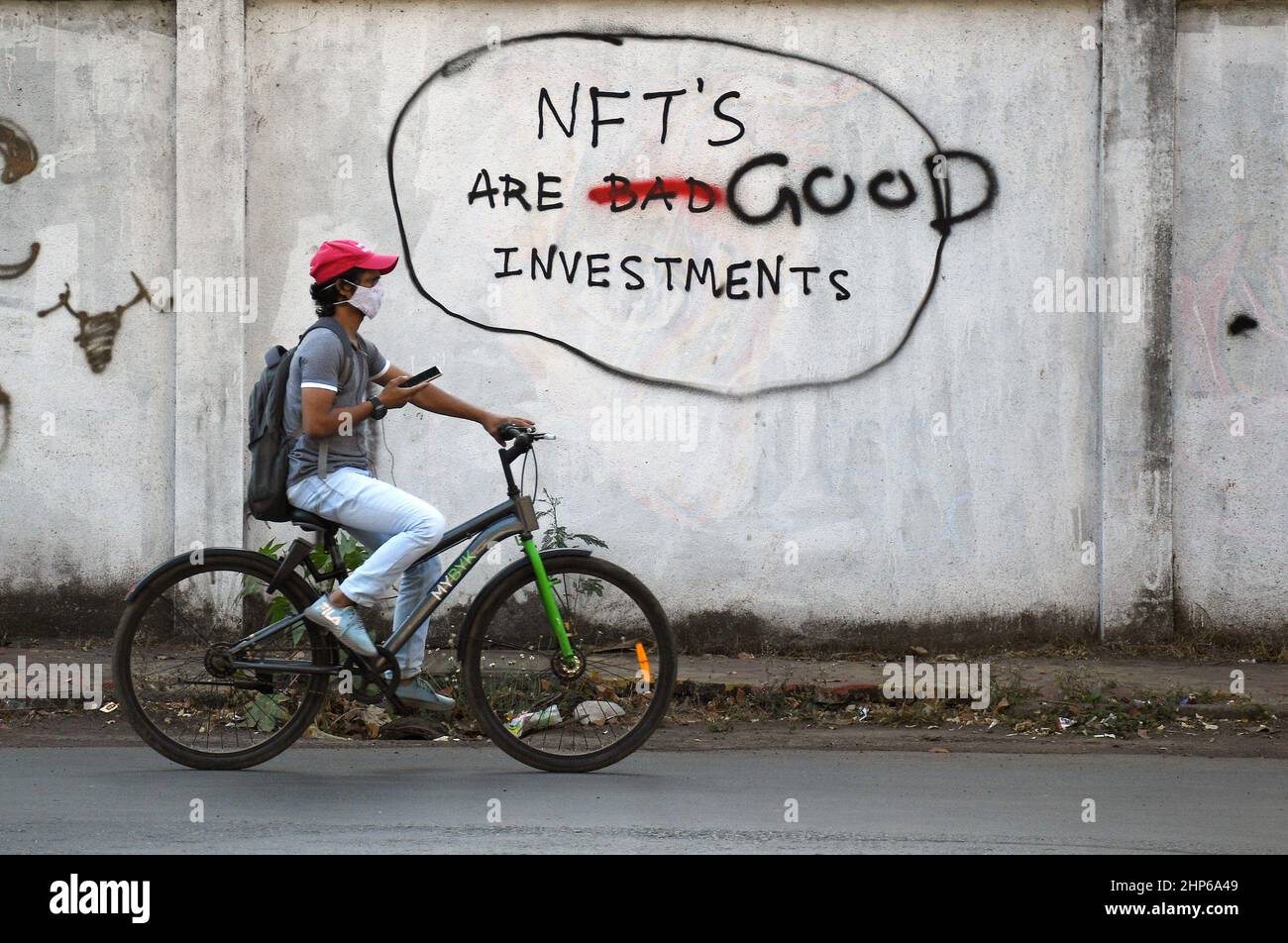 Mumbai, Indien. 18th. Februar 2022. Ein Mann mit einer schützenden Gesichtsmaske fährt mit dem Fahrrad an einem Graffiti vorbei, das auf einer Wand mit der Aufschrift „NFT's are Good Investments“ in Mumbai gemalt ist.Non fungible Tokens (NFT) sind digitale Vermögenswerte, die reale Objekte wie Kunst, Musik, Fotos usw. Es ermöglicht dem Käufer, den Originalartikel mit digitalen Rechten zu besitzen. (Foto von Ashish Vaishnav/SOPA Images/Sipa USA) Quelle: SIPA USA/Alamy Live News Stockfoto